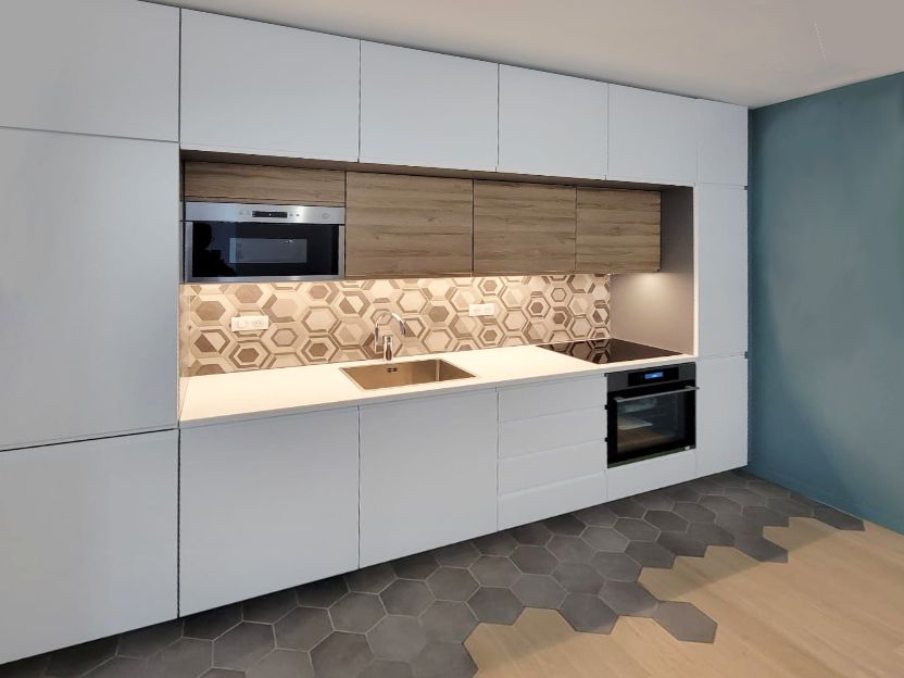 Cuisine linéaire aux façades blanches et bois, crédence en carreaux hexagonaux et sol tomettes grises et chêne, rénovée par un architecte d'intérieur.