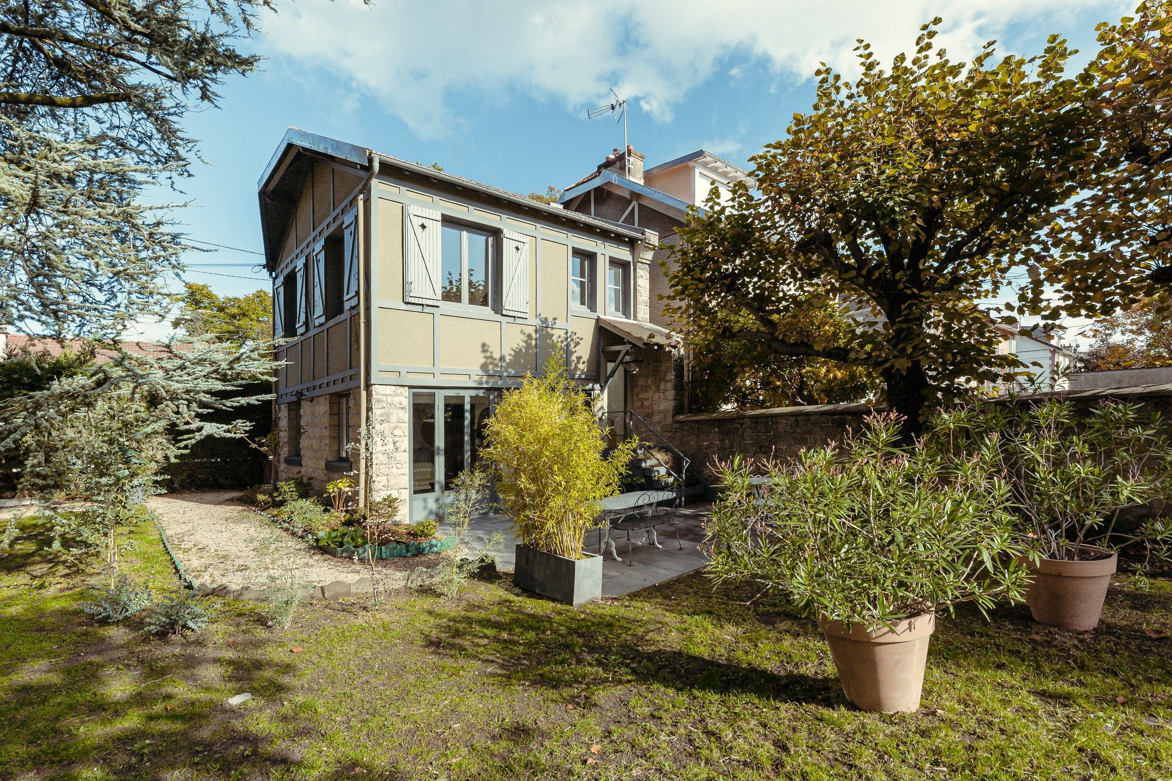 Façade arrière d'une maison de ville à étage avec extension en pierre meulière et bardage bois sur jardin planté d'oliviers, rénovation de maison.