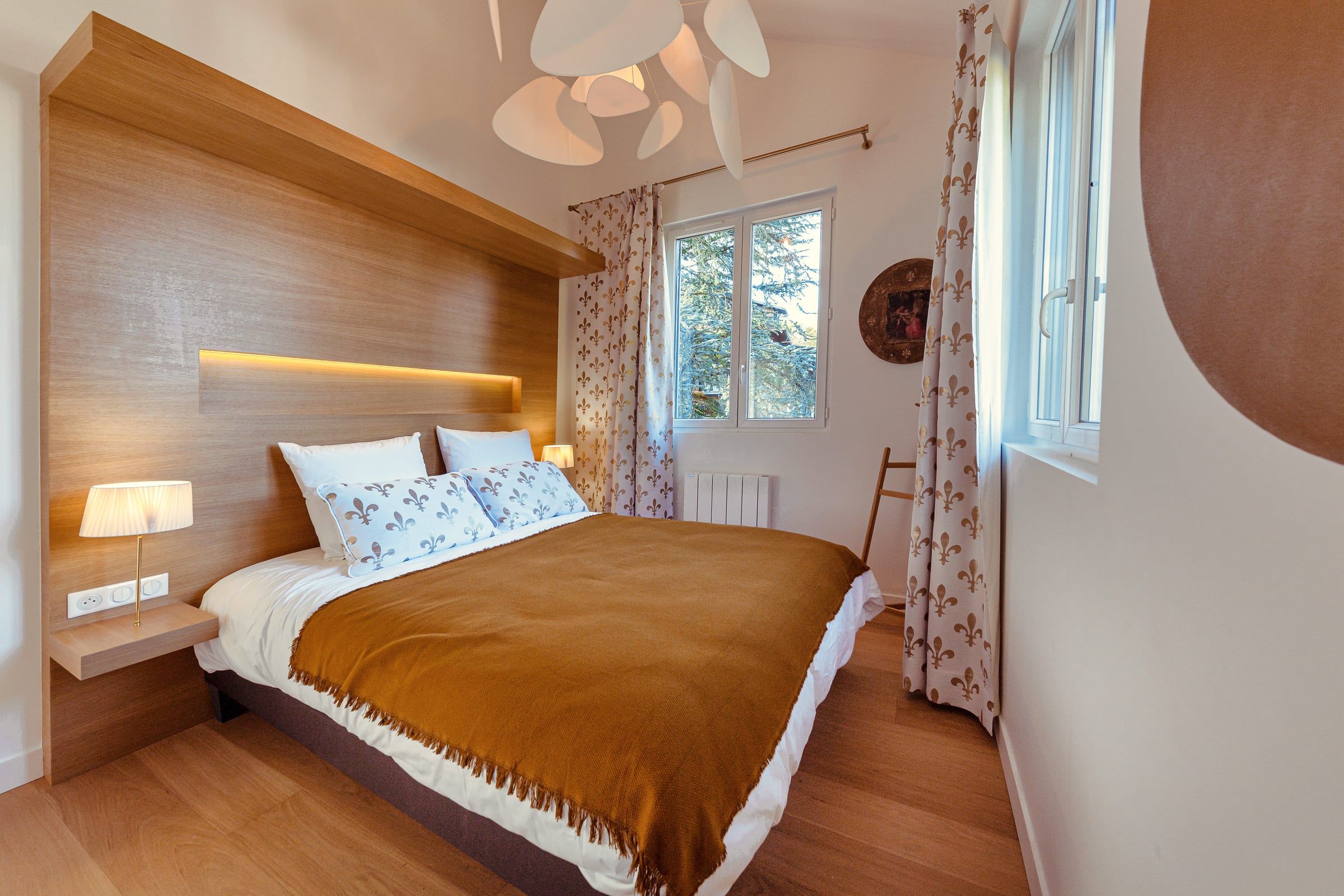 Chambre avec tête de lit en panneau de chêne et éclairage indirect, parquet chêne, plaid ocre et rideaux à motifs, agencement sur mesure contemporain.