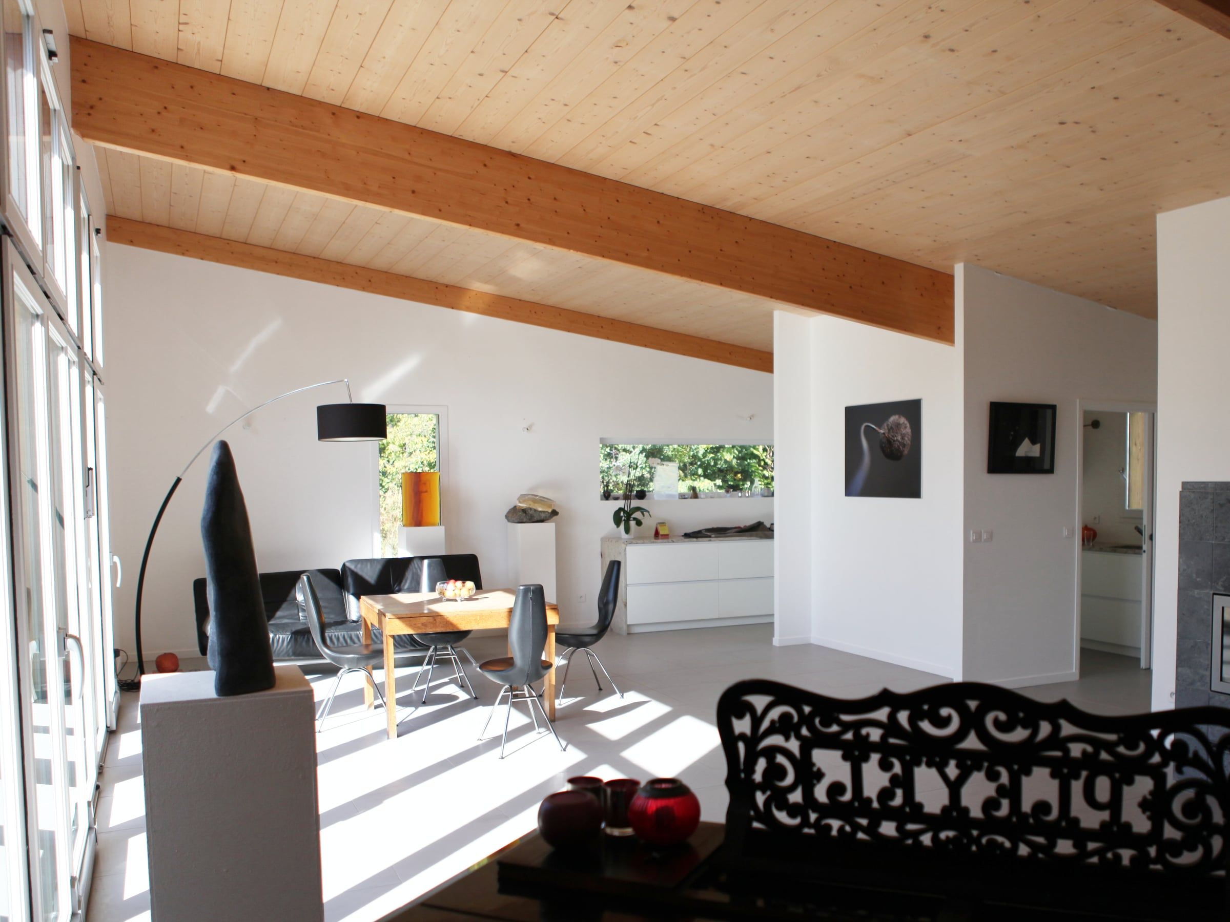 Maison contemporaine conçue par un architecte d’intérieur, avec séjour ouvert, plafond et poutres en bois, baies vitrées et sol carrelé clair.