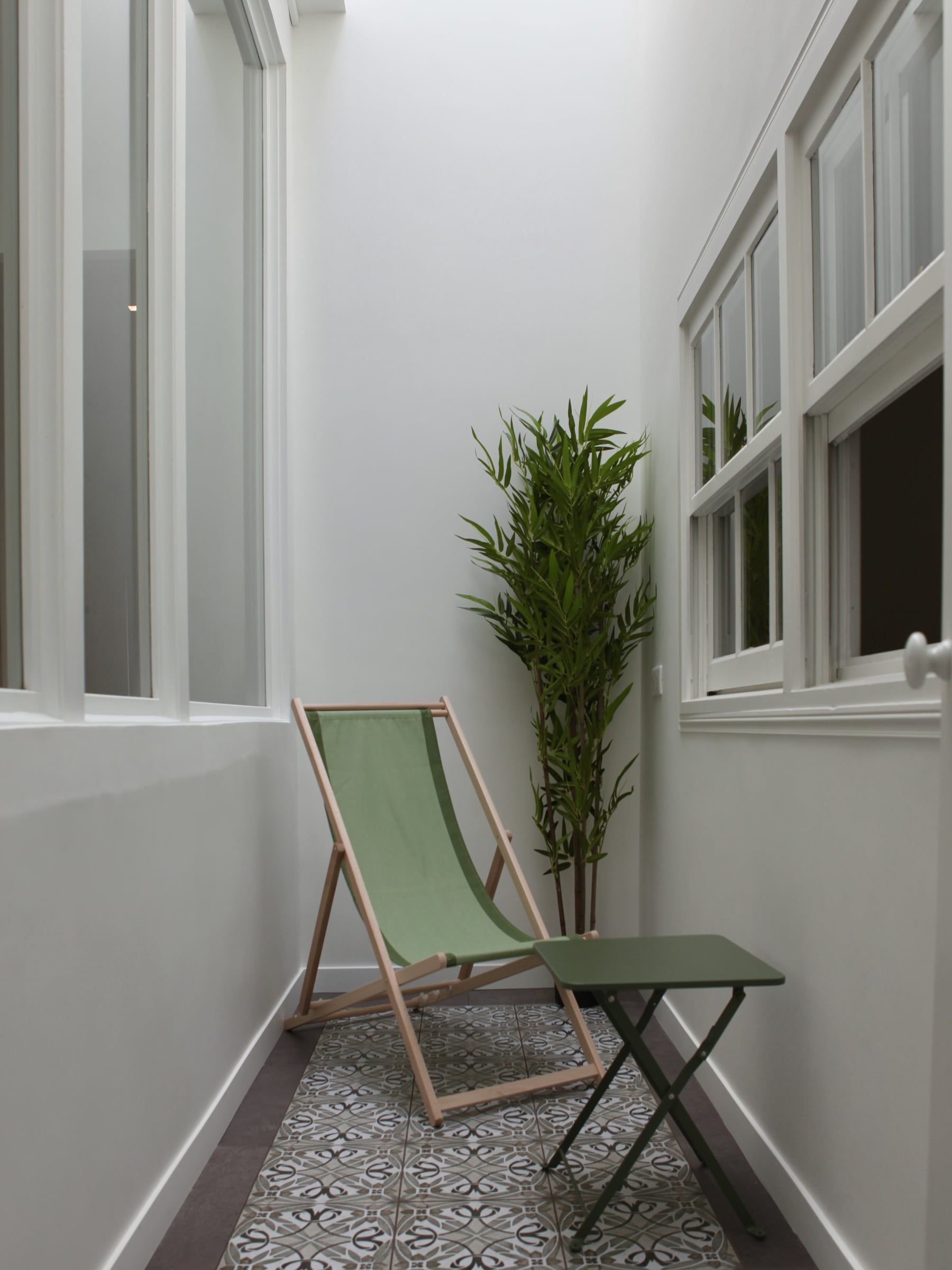 Patio sous verrière aux murs blancs, sol en carreaux de ciment à motifs et bambou en pot, issu d'une création de verrière intérieure.