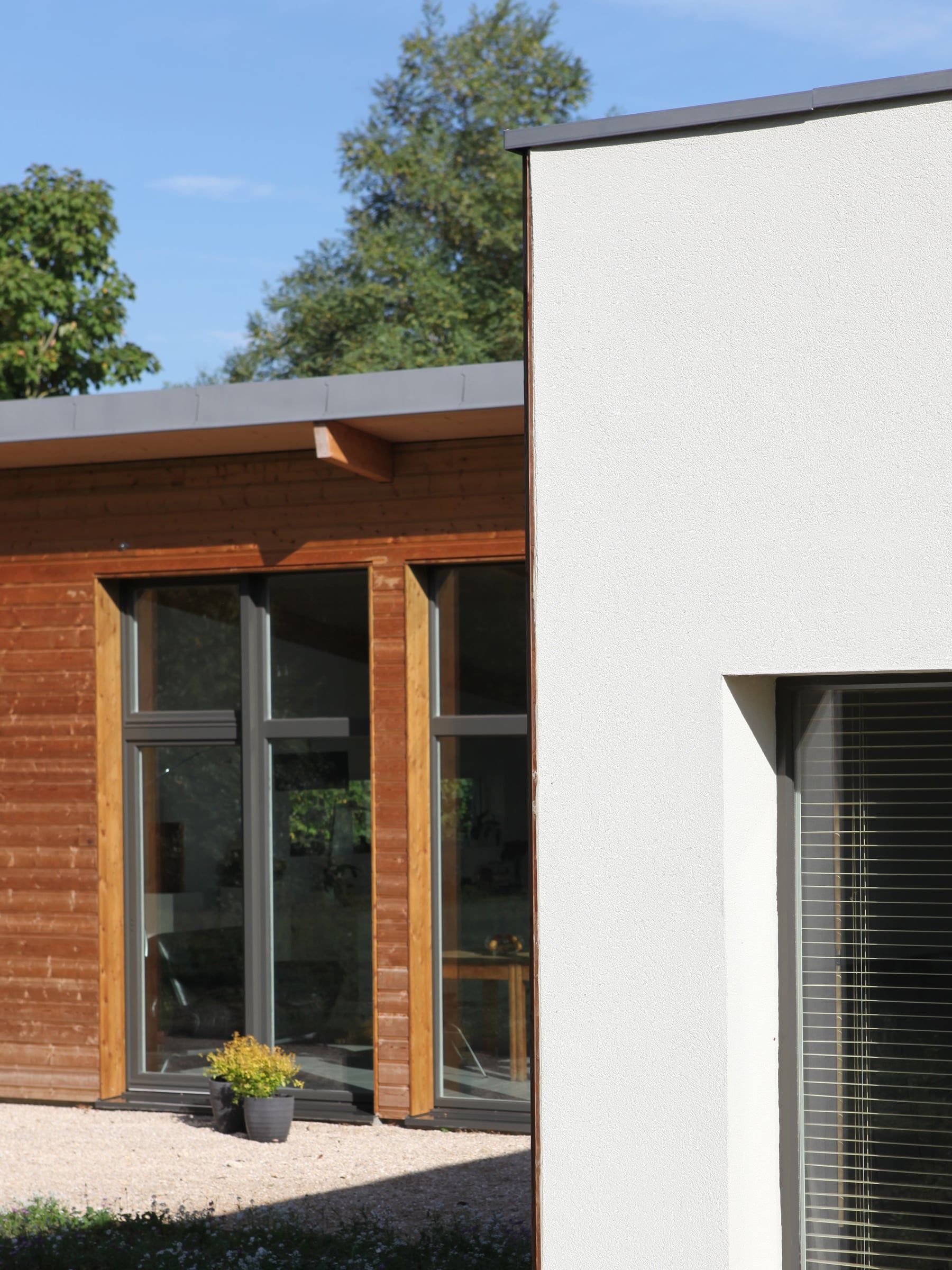 Extension résidentielle en bardage bois et enduit blanc, avec menuiseries anthracite toute hauteur et toiture plate à rive métallique.