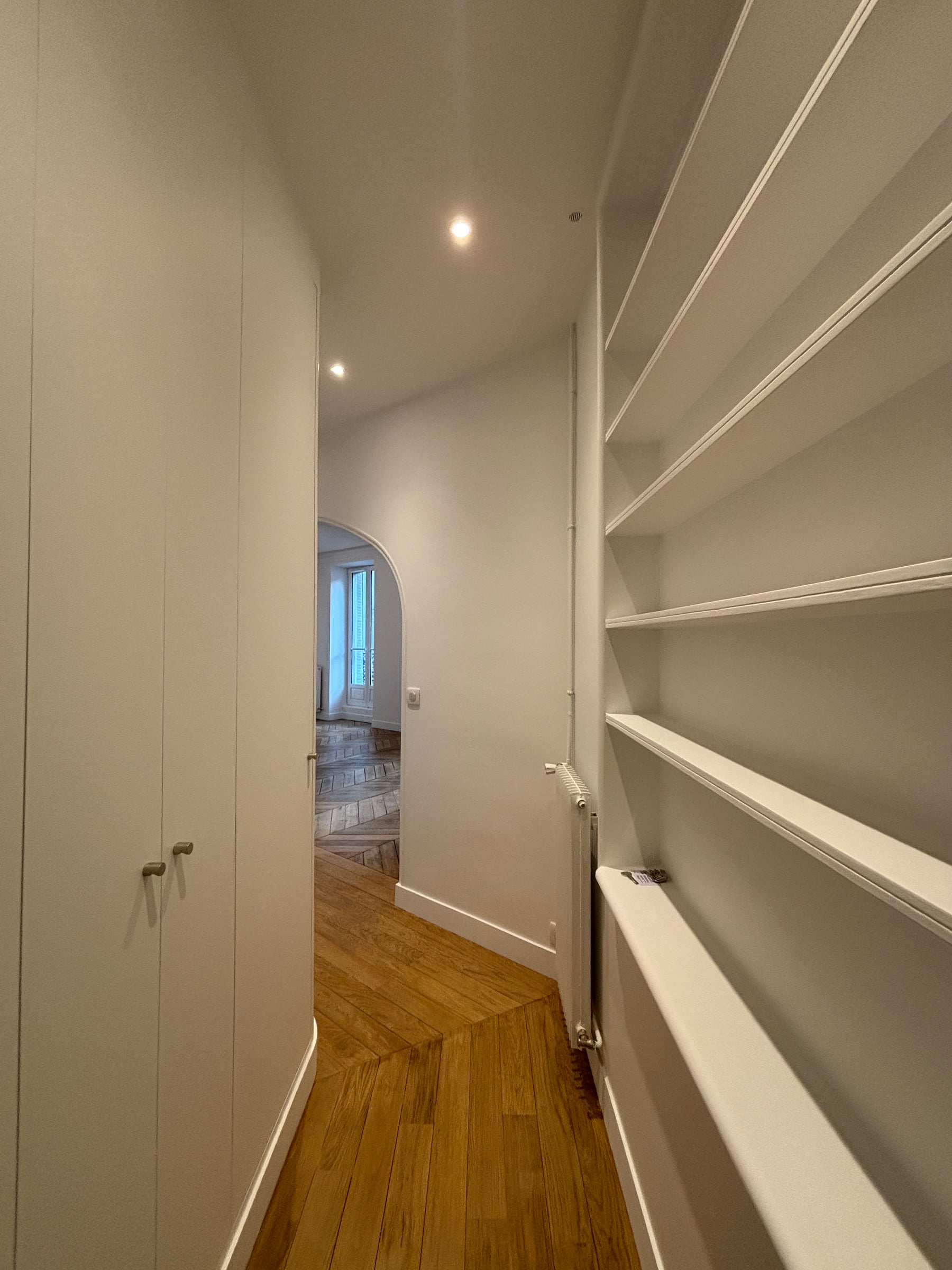 Séjour haussmannien aux poutres apparentes blanches et parquet point de Hongrie, ouvert sur une pièce voûtée après rénovation d'appartement.