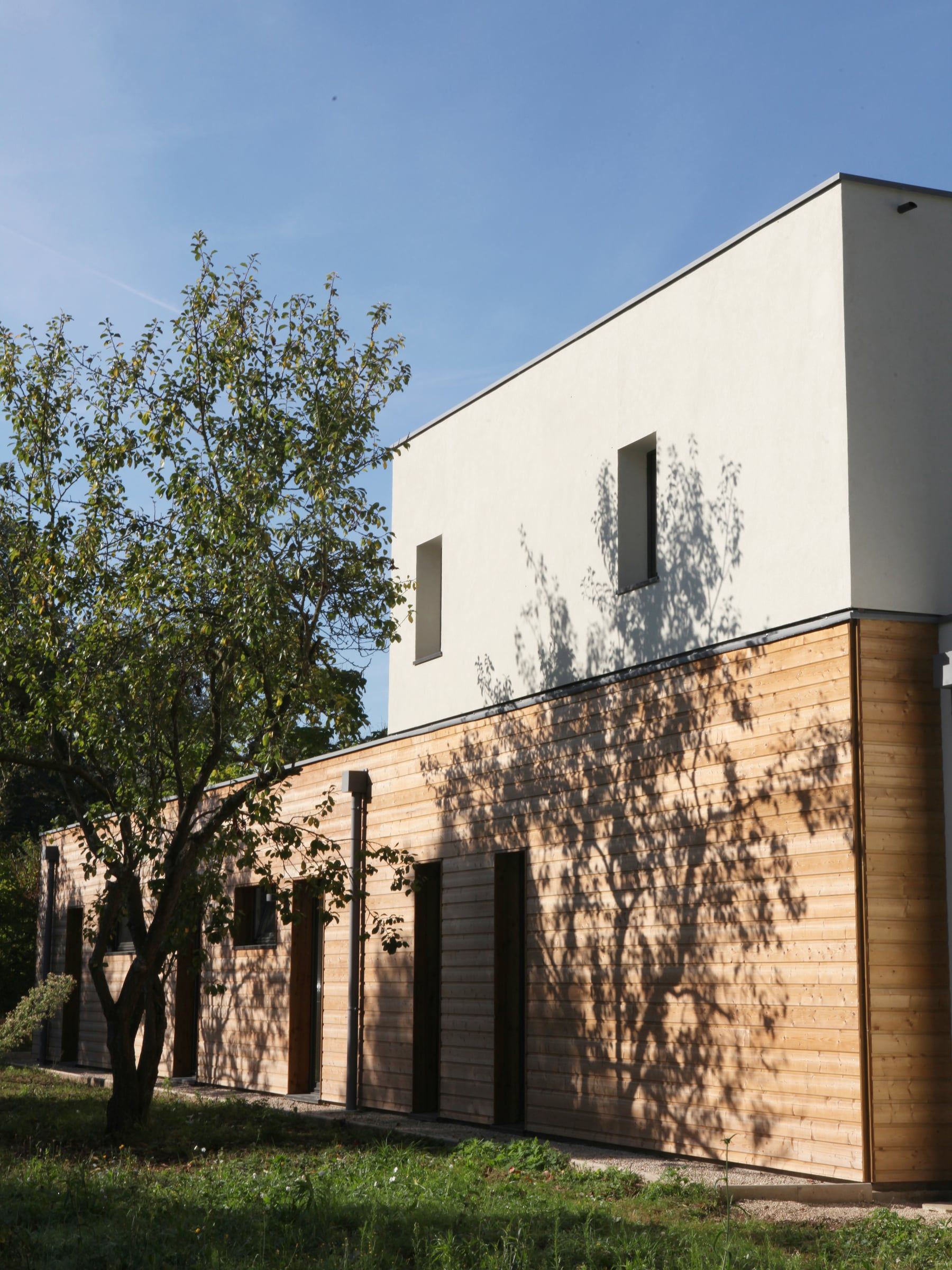 Façade de maison contemporaine associant bardage horizontal en bois et volume supérieur enduit blanc, rythmée par des fenêtres étroites.