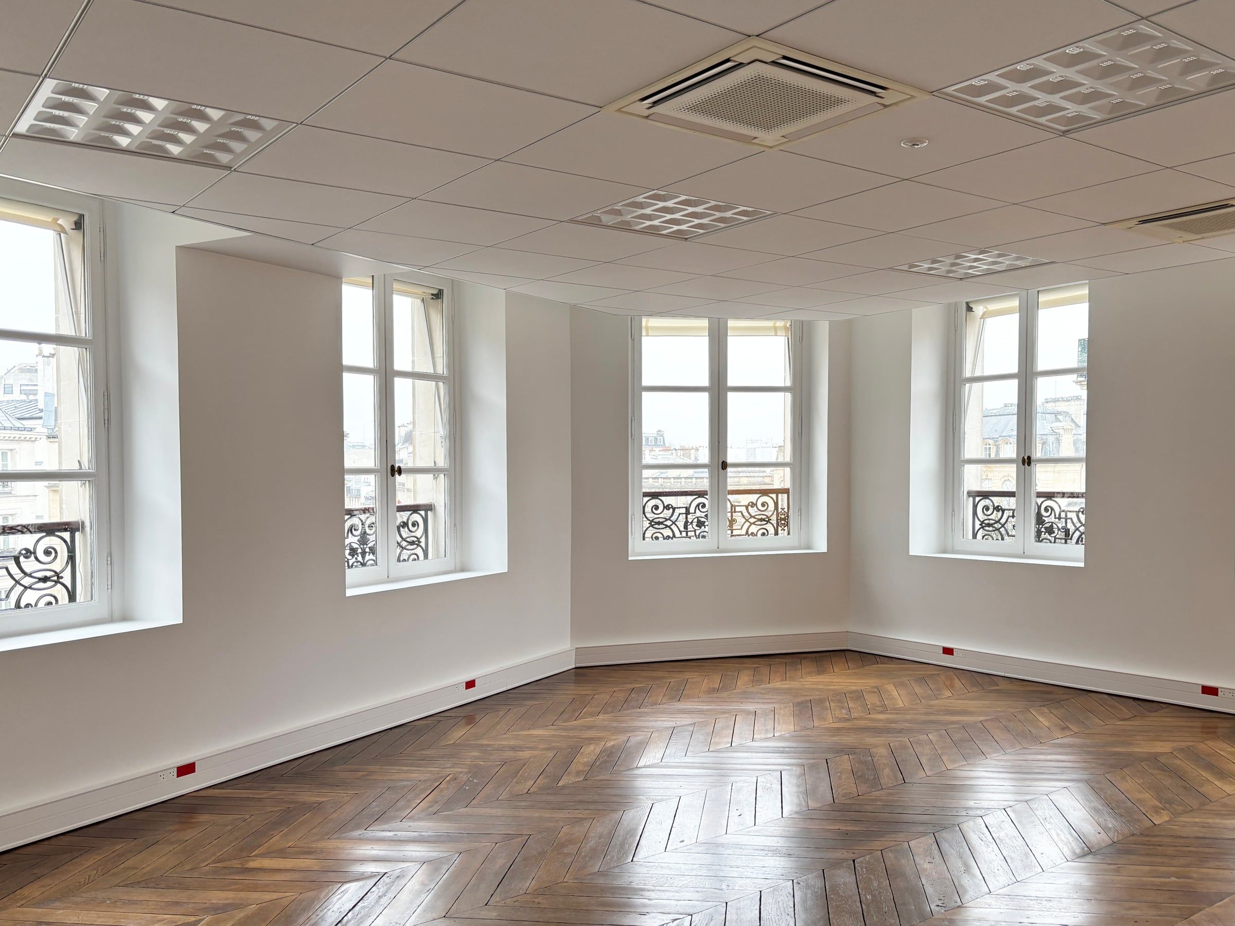 Plateau de bureaux haussmannien rénové, parquet en point de Hongrie, bow-window et garde-corps en fer forgé, espace de travail lumineux