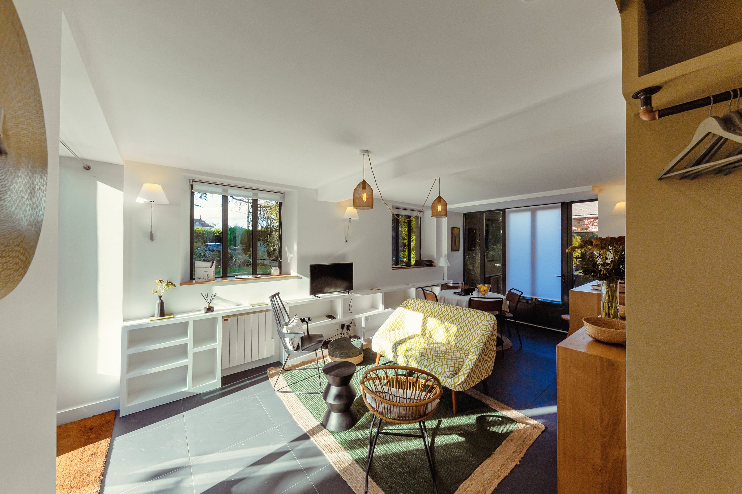 Séjour ouvert sur le jardin avec fauteuils en rotin, tapis en jute et suspensions tressées baignés de lumière naturelle, rénovation d'appartement.