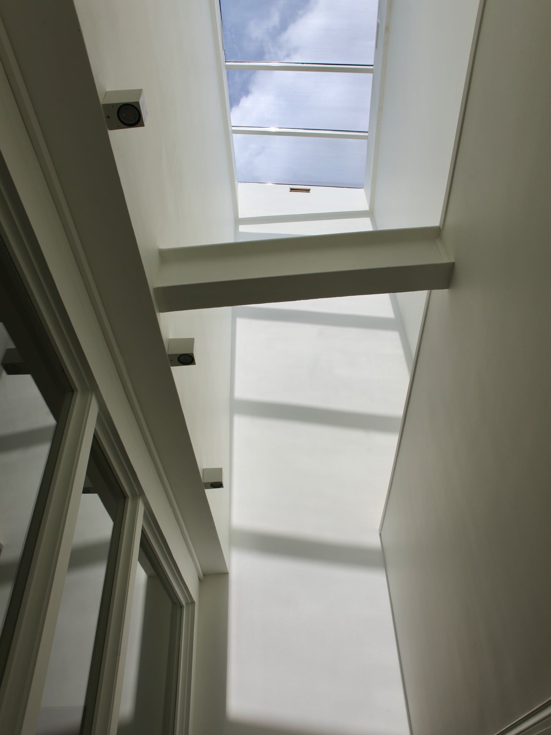 Contre-plongée sur une verrière de toiture vitrée ouvrant sur le ciel, encadrée de murs blancs et parois vitrées, issue d'une création de verrière.