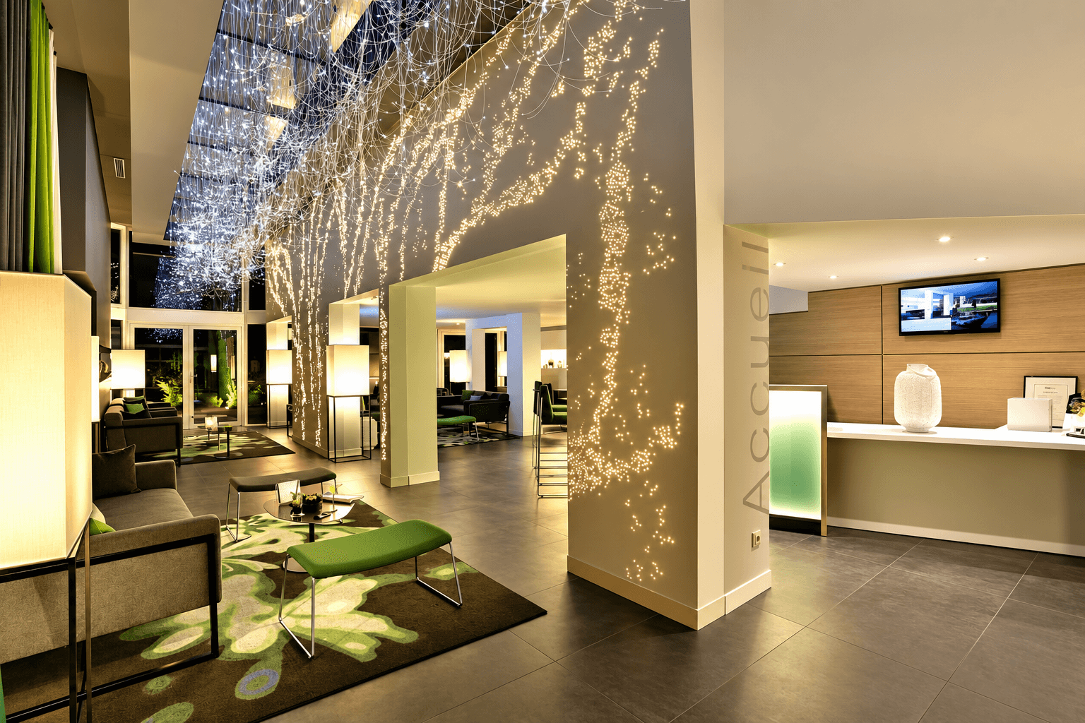 Hall d'accueil d'hôtel rénové par un architecte d'intérieur, suspension de fibres optiques en cascade, mobilier vert anis et sol en grès cérame gris.