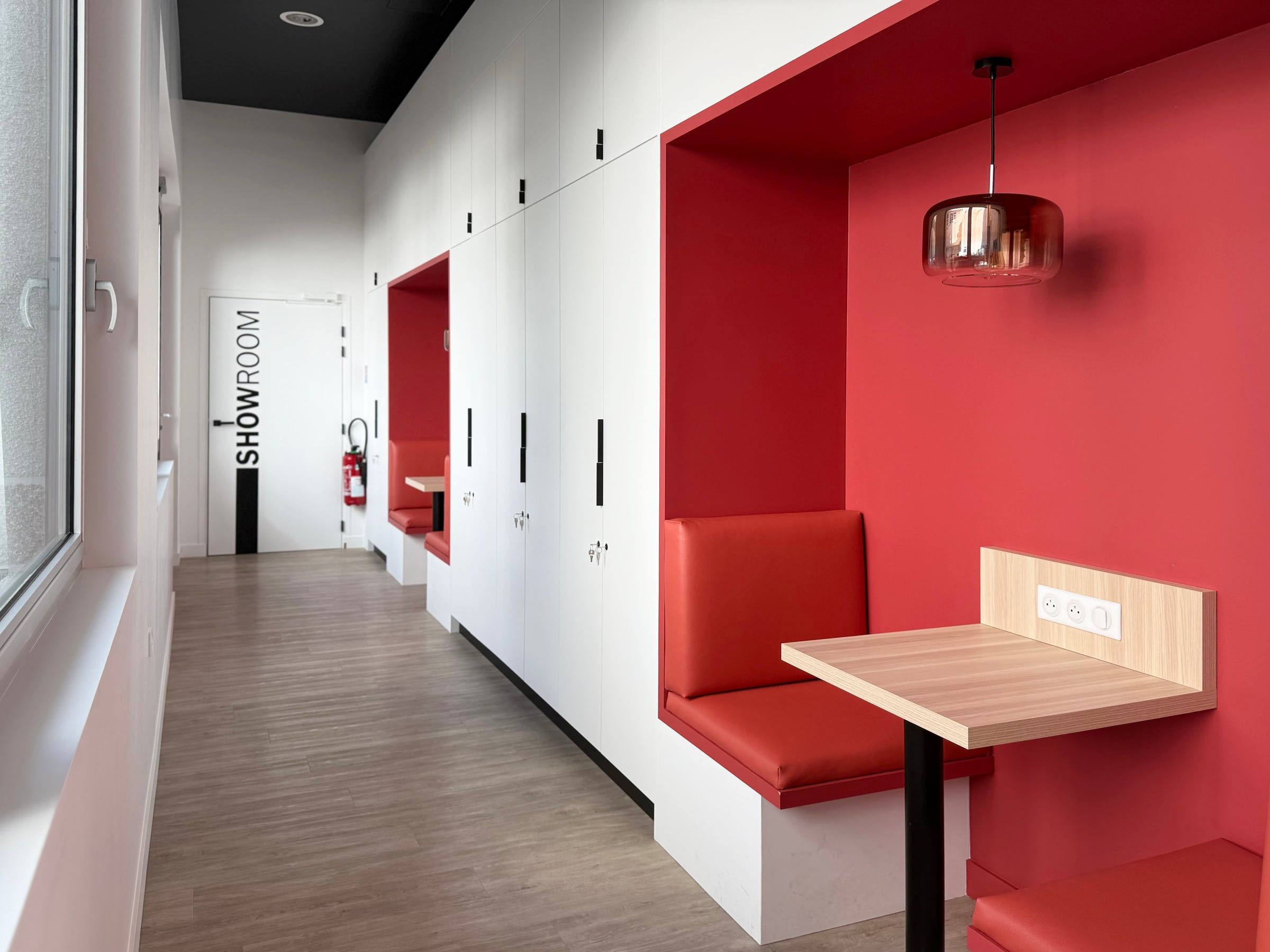 Showroom et aménagement de bureaux par un architecte d'intérieur : alcôves capitonnées en cuir rouge, rangements blancs, sol bois et plafond noir.
