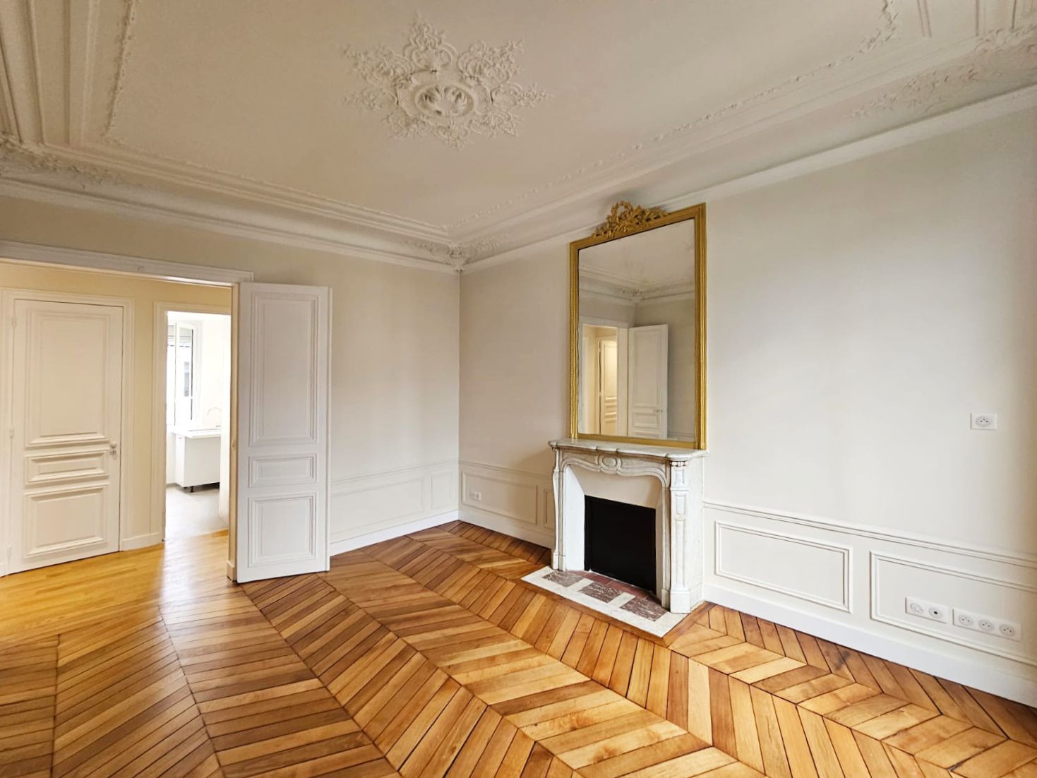 Salon haussmannien aux moulures et rosace en plâtre, cheminée en marbre à trumeau doré et parquet en point de Hongrie rénové par un architecte d'intérieur.