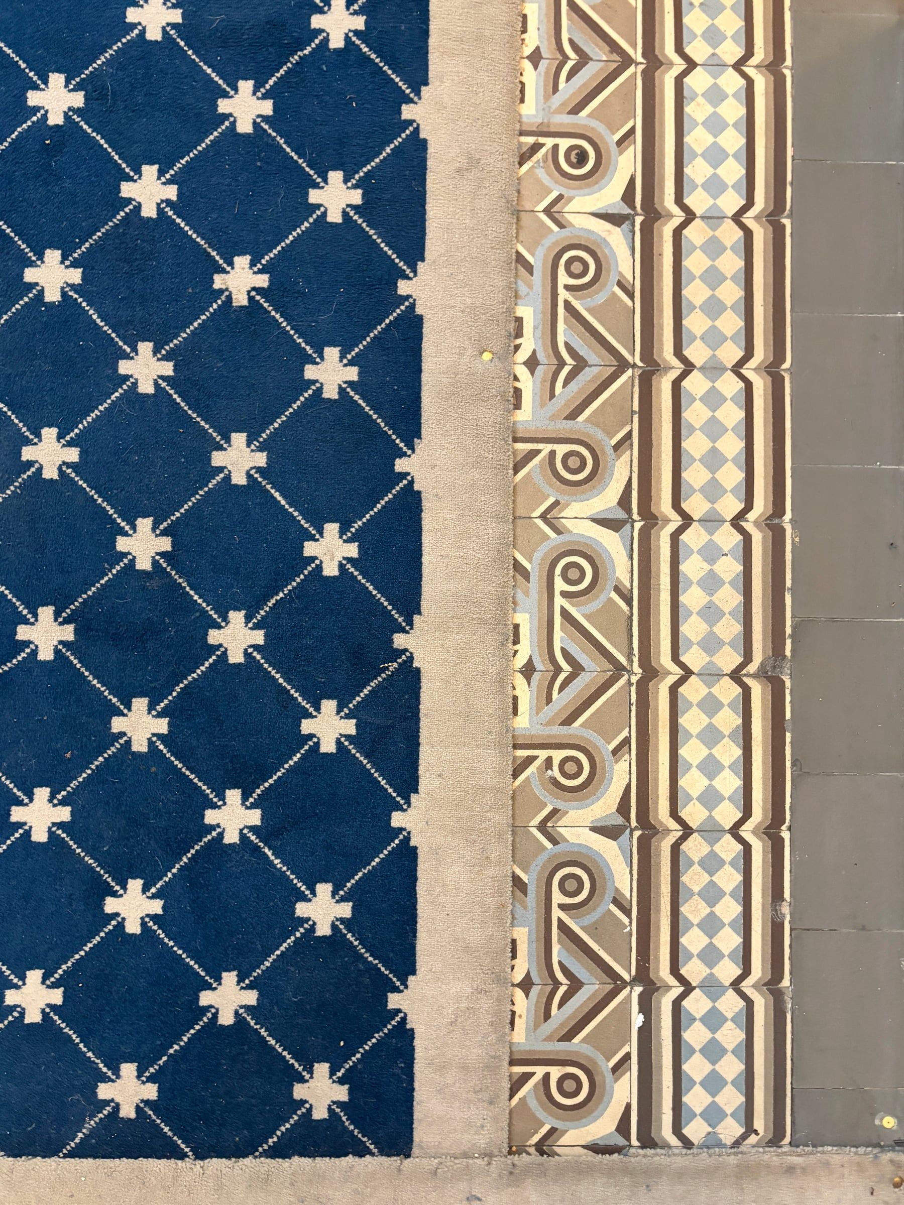 Détail de la jonction entre tapis bleu à motifs écrus, carreaux anciens à dessins géométriques et sol en dalles grises.