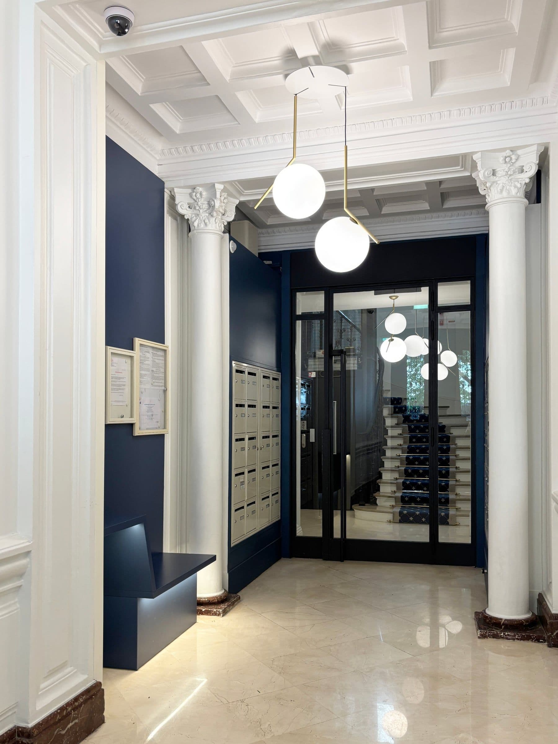 Après travaux : hall restauré avec colonnes à chapiteaux, plafond à caissons, boîtes aux lettres encastrées et cloison bleu nuit.