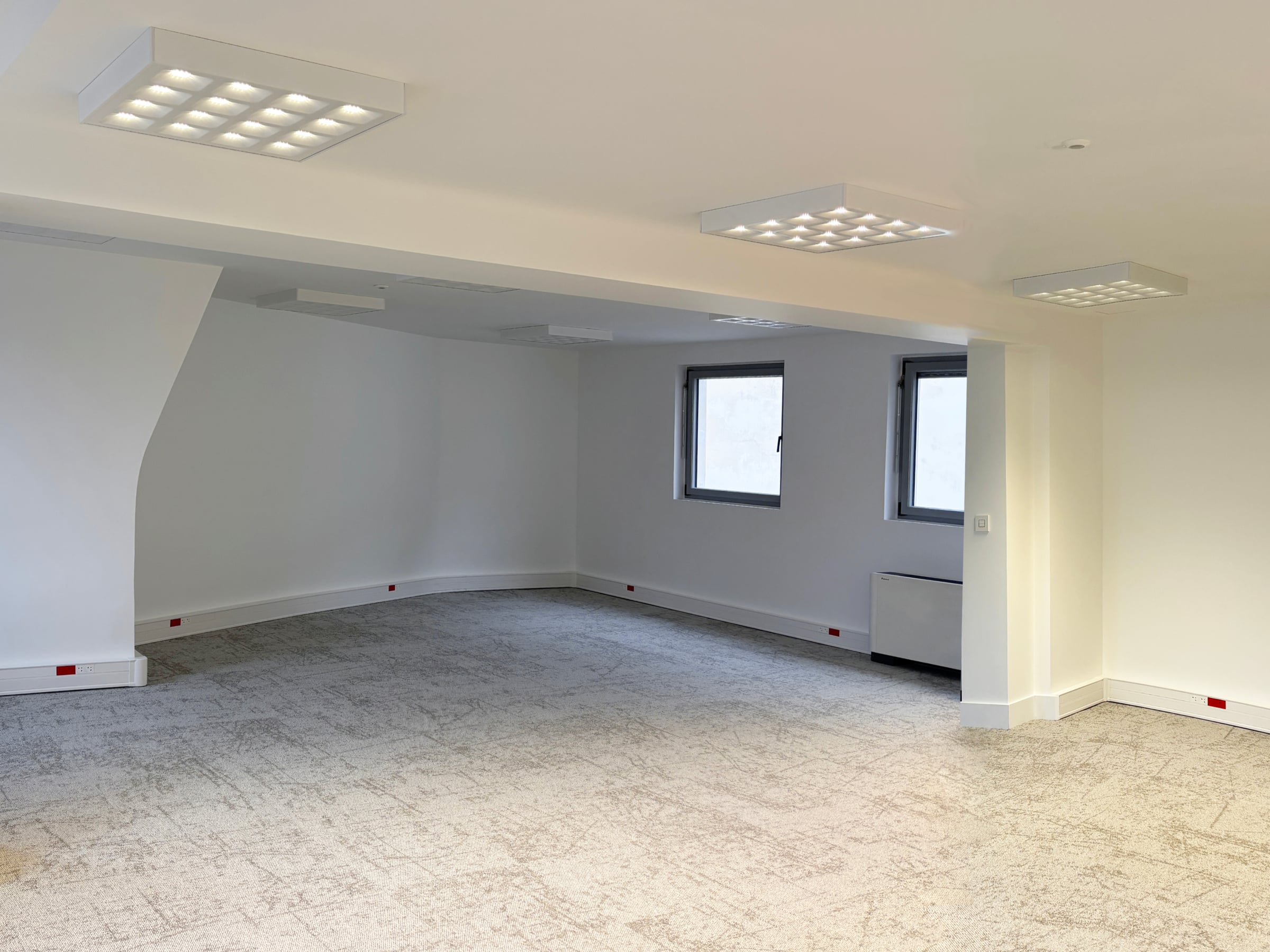Plateau de bureaux ouvert sous combles avec moquette claire, dalles lumineuses au plafond et fenêtres de toit, espace de travail décloisonné