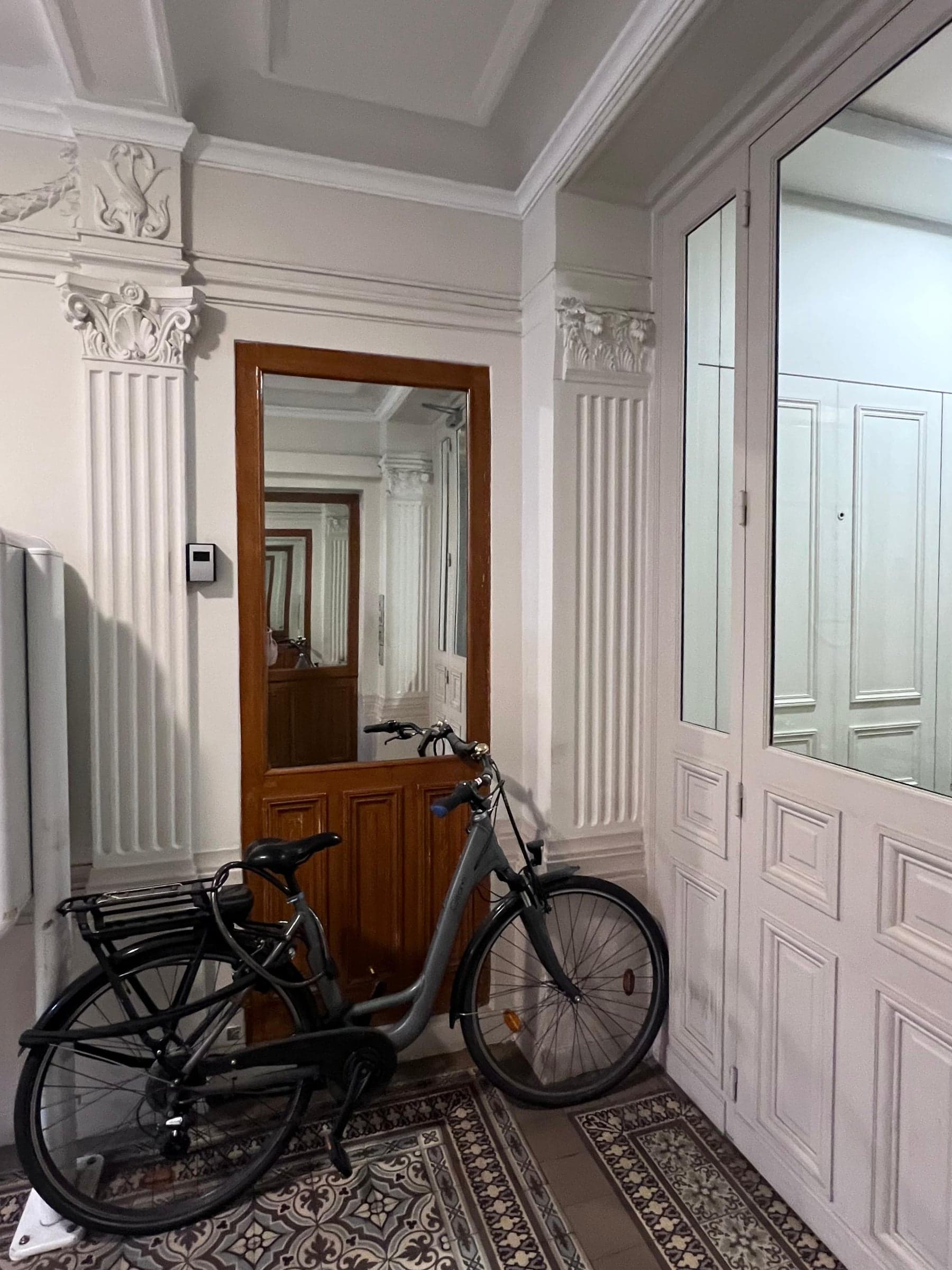 Avant travaux : porte palière grise à panneaux moulurés, boiseries d'origine, parquet ancien et tapis d'escalier bleu, vue rapprochée du palier.