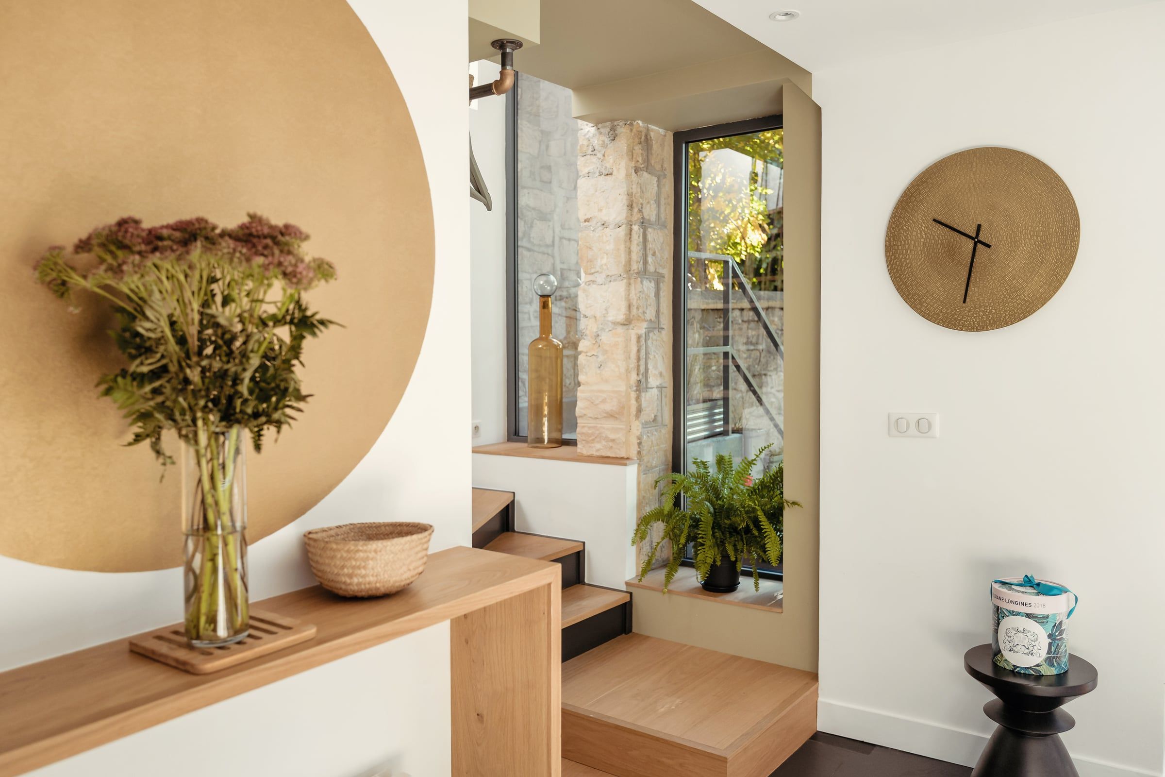 Entrée contemporaine avec console et emmarchement en chêne, mur enduit ocre, verrière acier sur cour pavée et horloge en laiton, par un architecte d'intérieur.