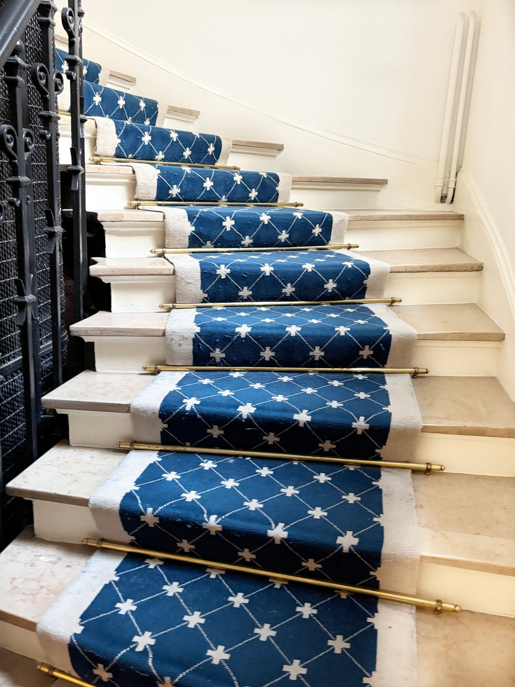 Réfection de cage d’escalier en pierre claire, habillée d’un tapis bleu à motifs géométriques et de tringles en laiton.