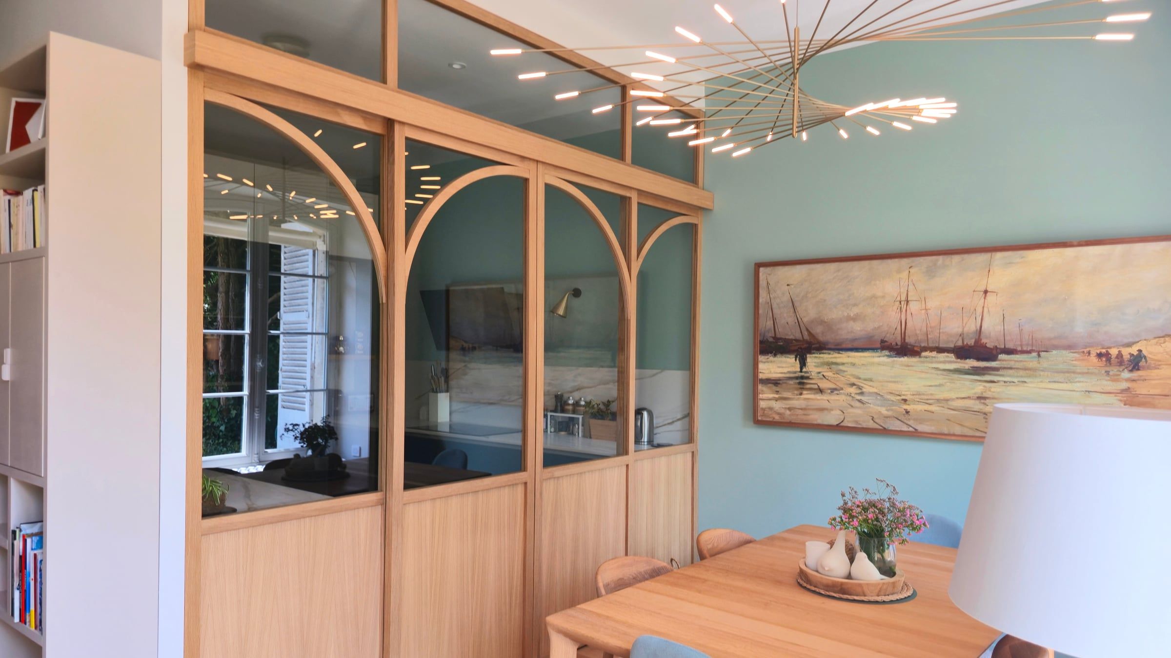 Salle à manger d’une maison rénovée par un architecte d’intérieur, séparée de la cuisine par une verrière en bois aux arcs cintrés.