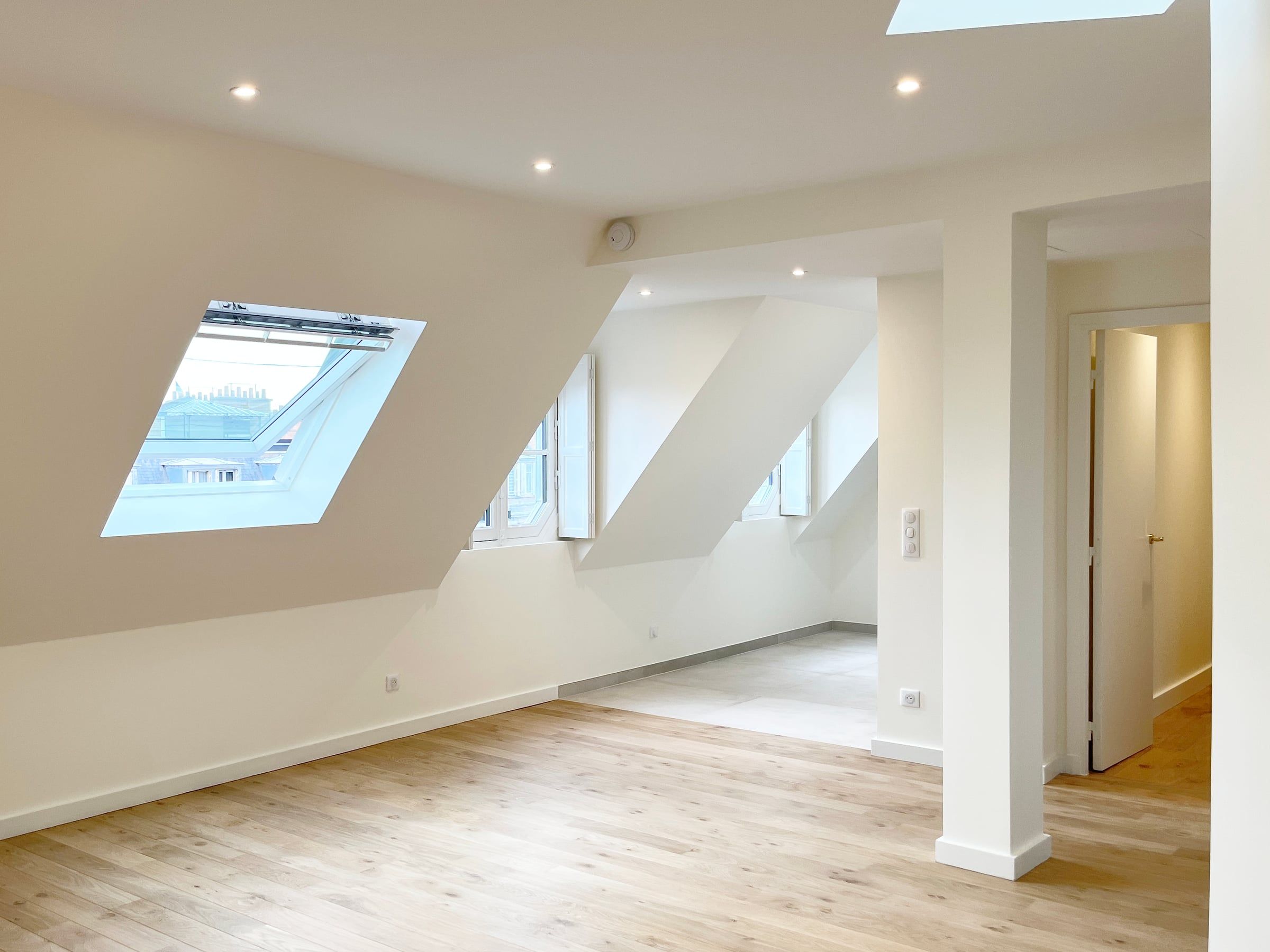 Séjour sous combles aux murs blancs, parquet en chêne clair, fenêtres de toit et trémies, rénové par un architecte d'intérieur à Paris.