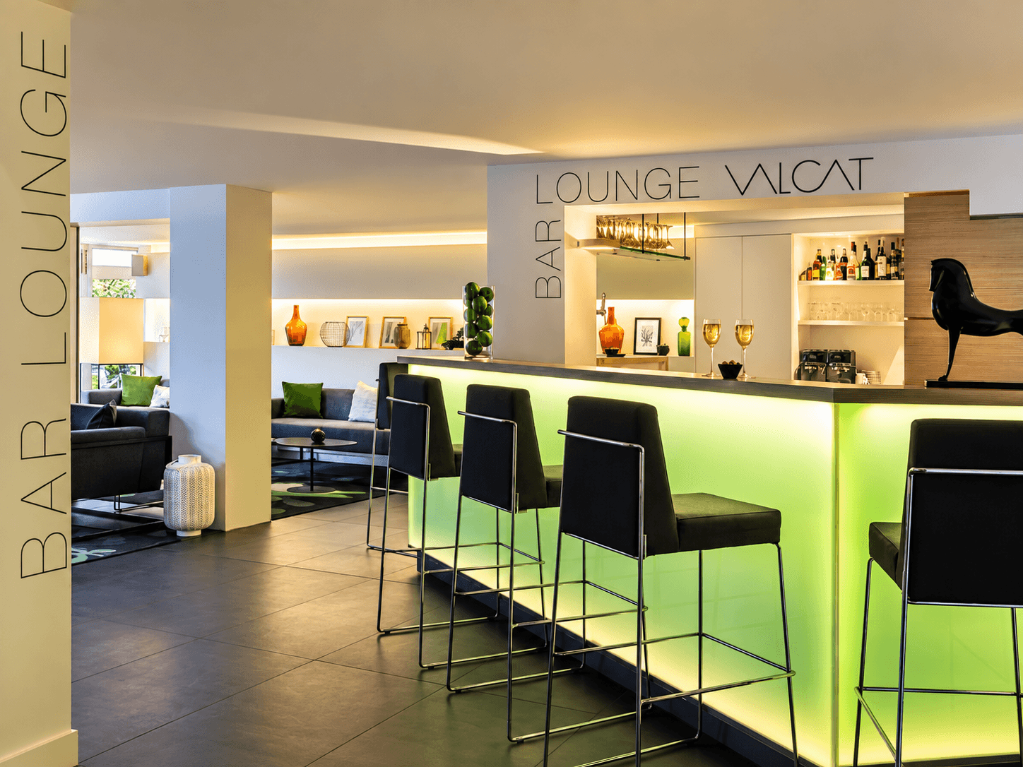 Bar lounge issu d'un projet d'architecture intérieure d'hôtel, comptoir rétroéclairé vert anis, tabourets hauts noirs et sculpture équine.