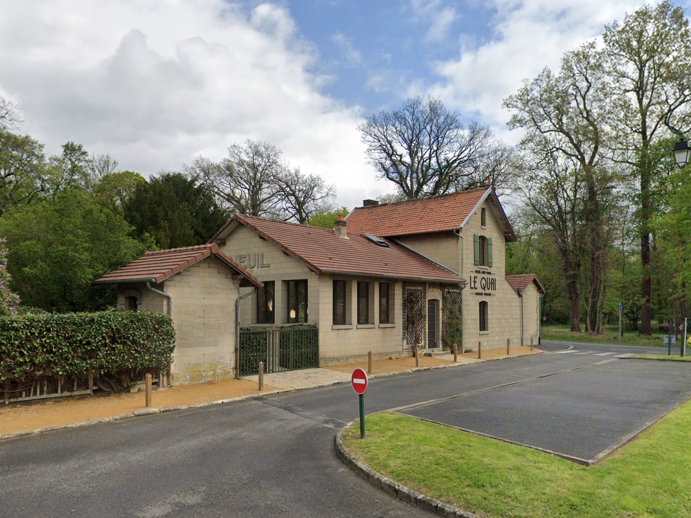 Façade en pierre de l'ancienne gare reconvertie en brasserie, toiture en tuiles et grilles en fer forgé, projet d'agencement de restaurant en lisière de forêt.