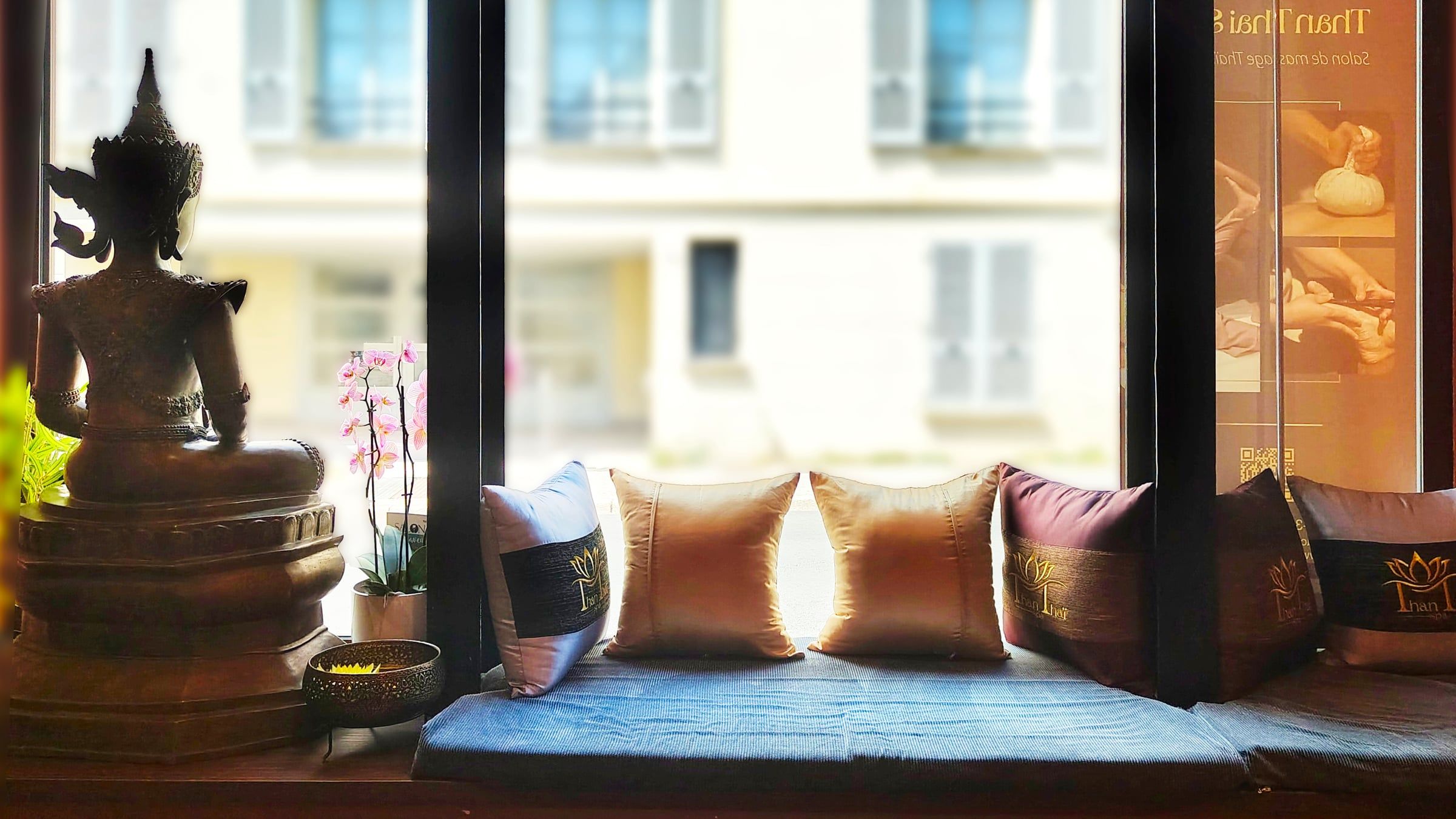 Espace d’accueil d’un spa rénové par un architecte d’intérieur, avec banquette sous fenêtre, statue bouddhique et coussins brodés.