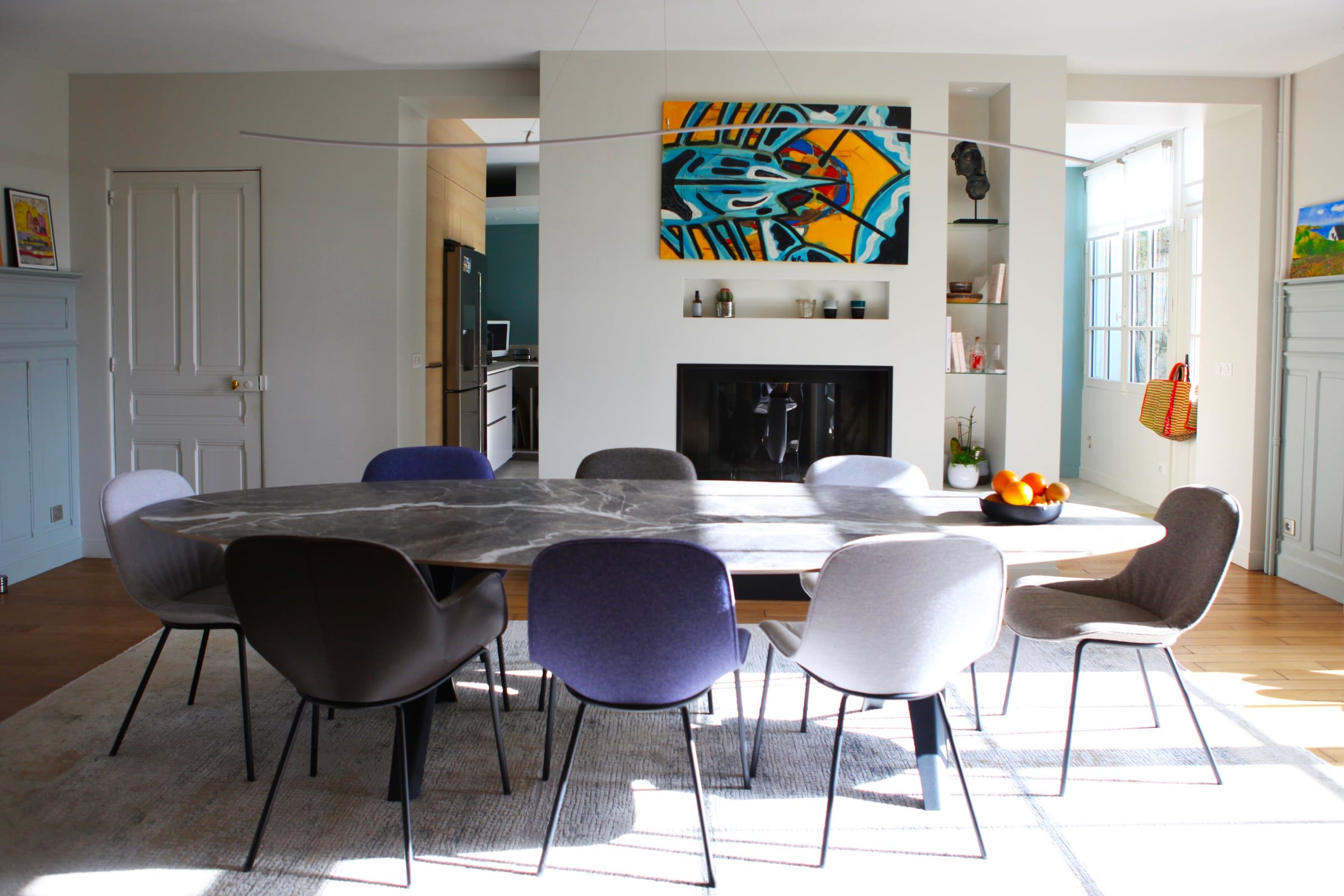 Salle à manger d’une maison résidentielle rénovée par un architecte d’intérieur, avec table en pierre sombre, cheminée encastrée et parquet.