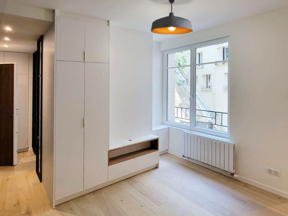 Pièce de vie avec rangements toute hauteur, banc en chêne, suspension noire et radiateur sous une fenêtre à garde-corps, rénovation d'appartement.