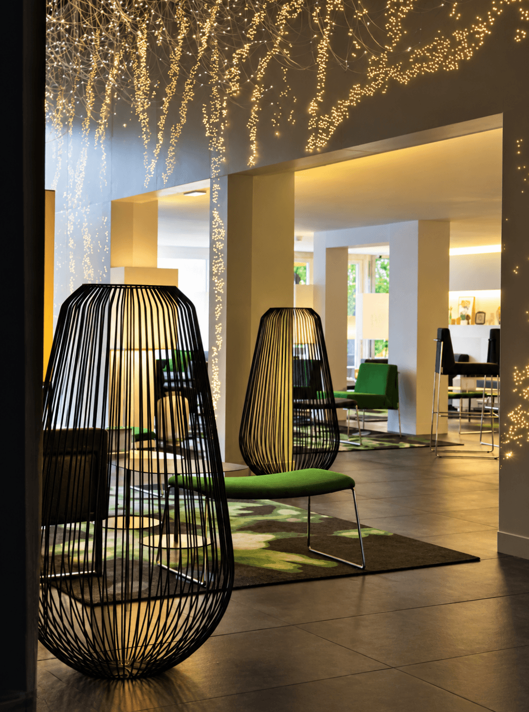 Coin lounge d'hôtel avec lampadaires cage en métal filaire noir, fauteuil vert et plafond de fibres optiques lumineuses.