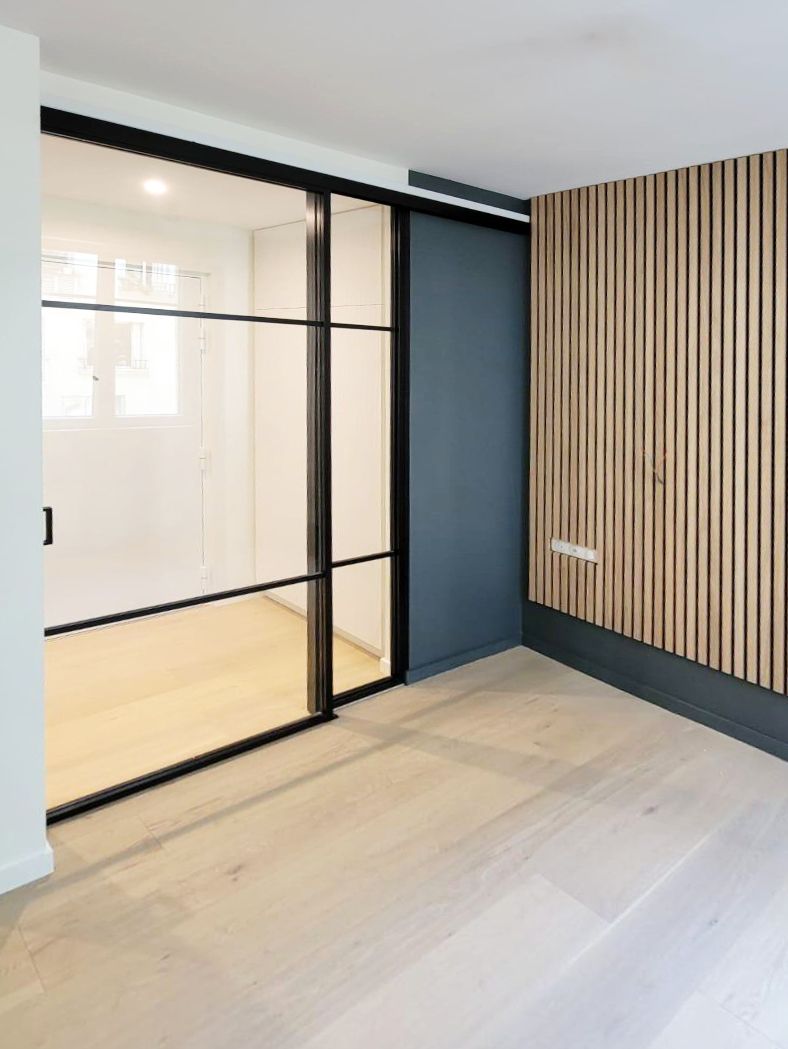Cloison verrière en acier noir et mur habillé de tasseaux de chêne sur fond bleu canard, parquet clair signé par une agence d'architecture intérieure.
