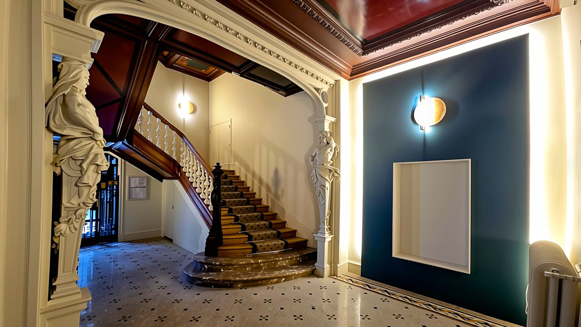 Hall d’immeuble historique rénové par un architecte d’intérieur, avec escalier en bois, mosaïque au sol, arche moulurée et éclairage intégré.