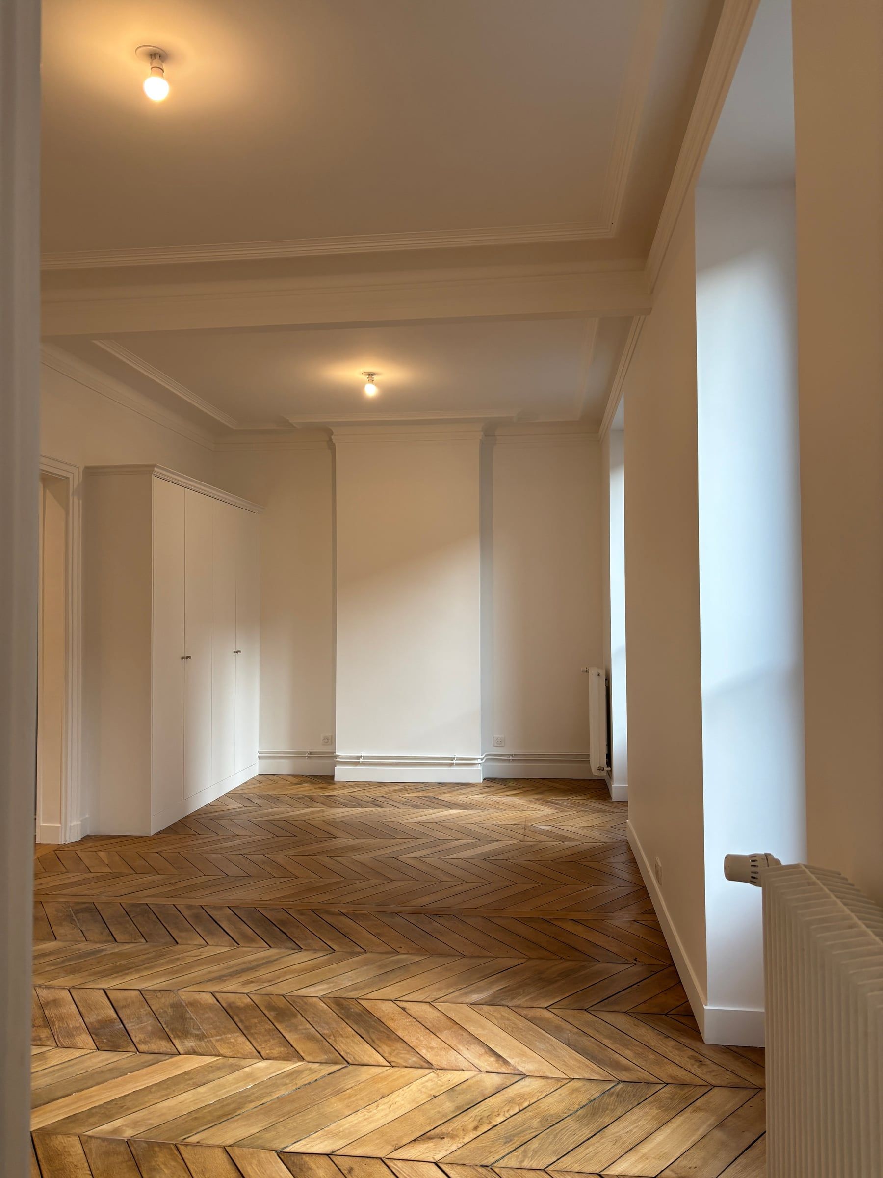 Pièce haussmannienne au parquet point de Hongrie et poutre apparente, niche voûtée à étagères éclairée par des appliques murales.