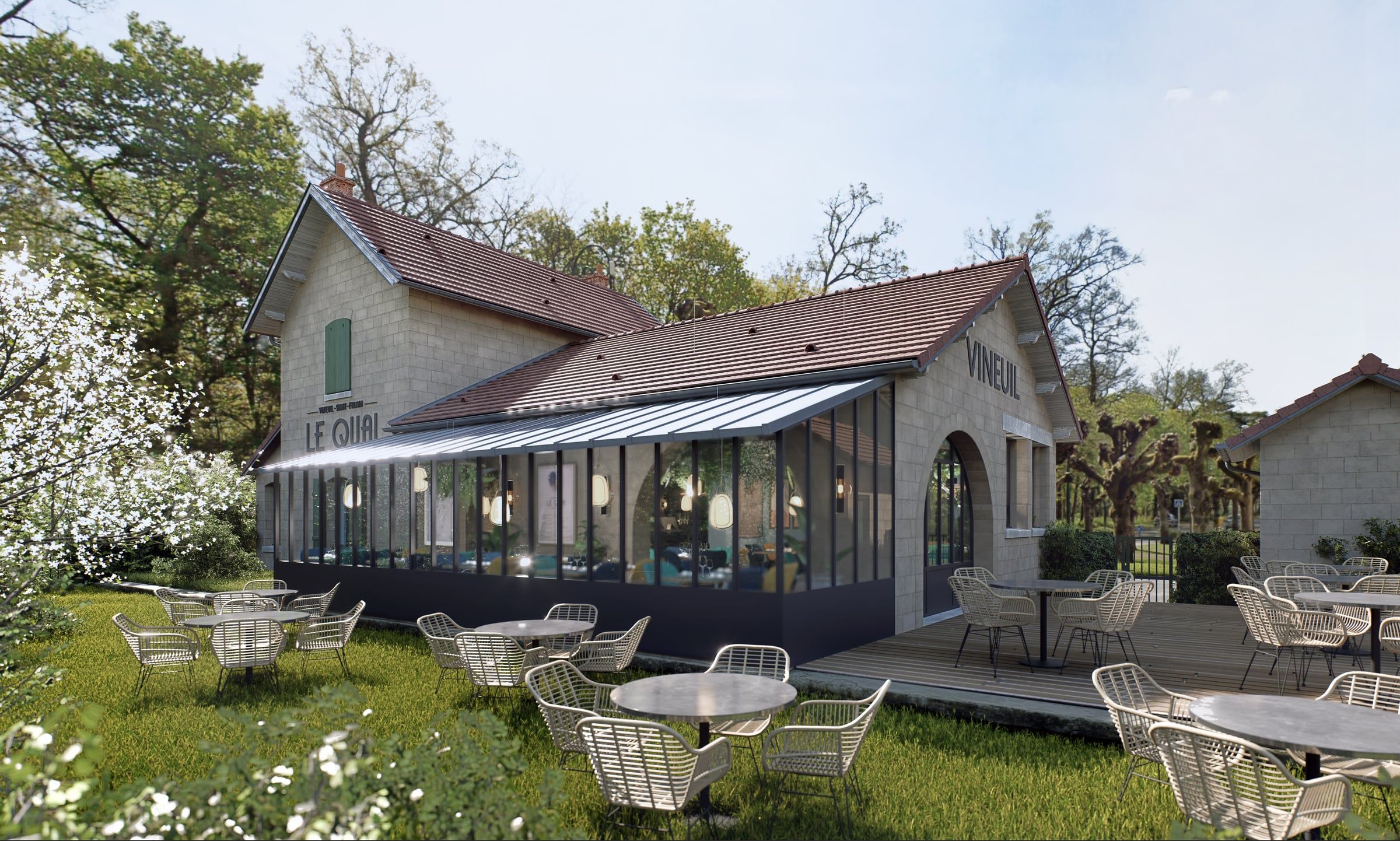 Façade latérale en pierre du restaurant Le Quai, longue verrière abritant la salle et terrasse en gravier aux guéridons métalliques au printemps.