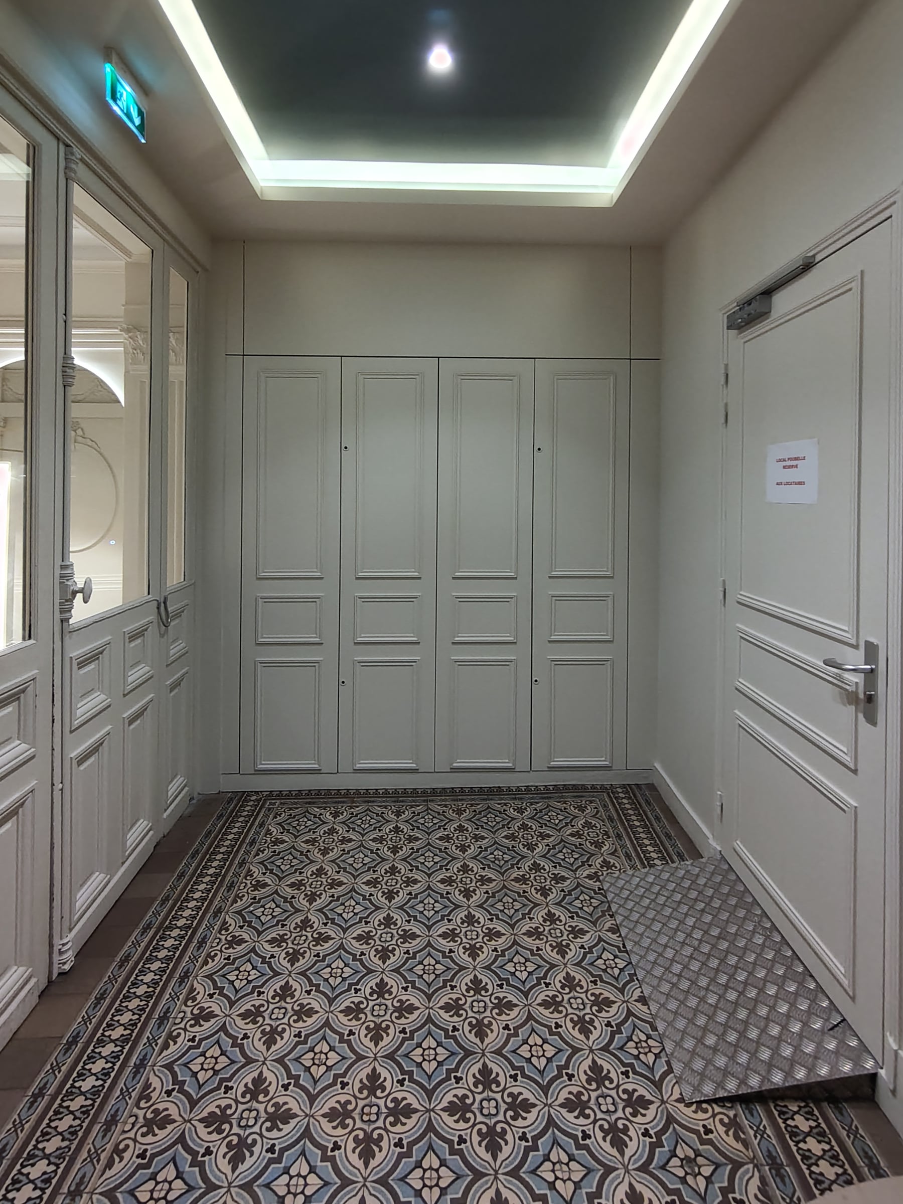 Couloir de distribution aux placards intégrés laqués et porte palière, sol en carreaux de ciment à motifs et faux plafond à corniche lumineuse.