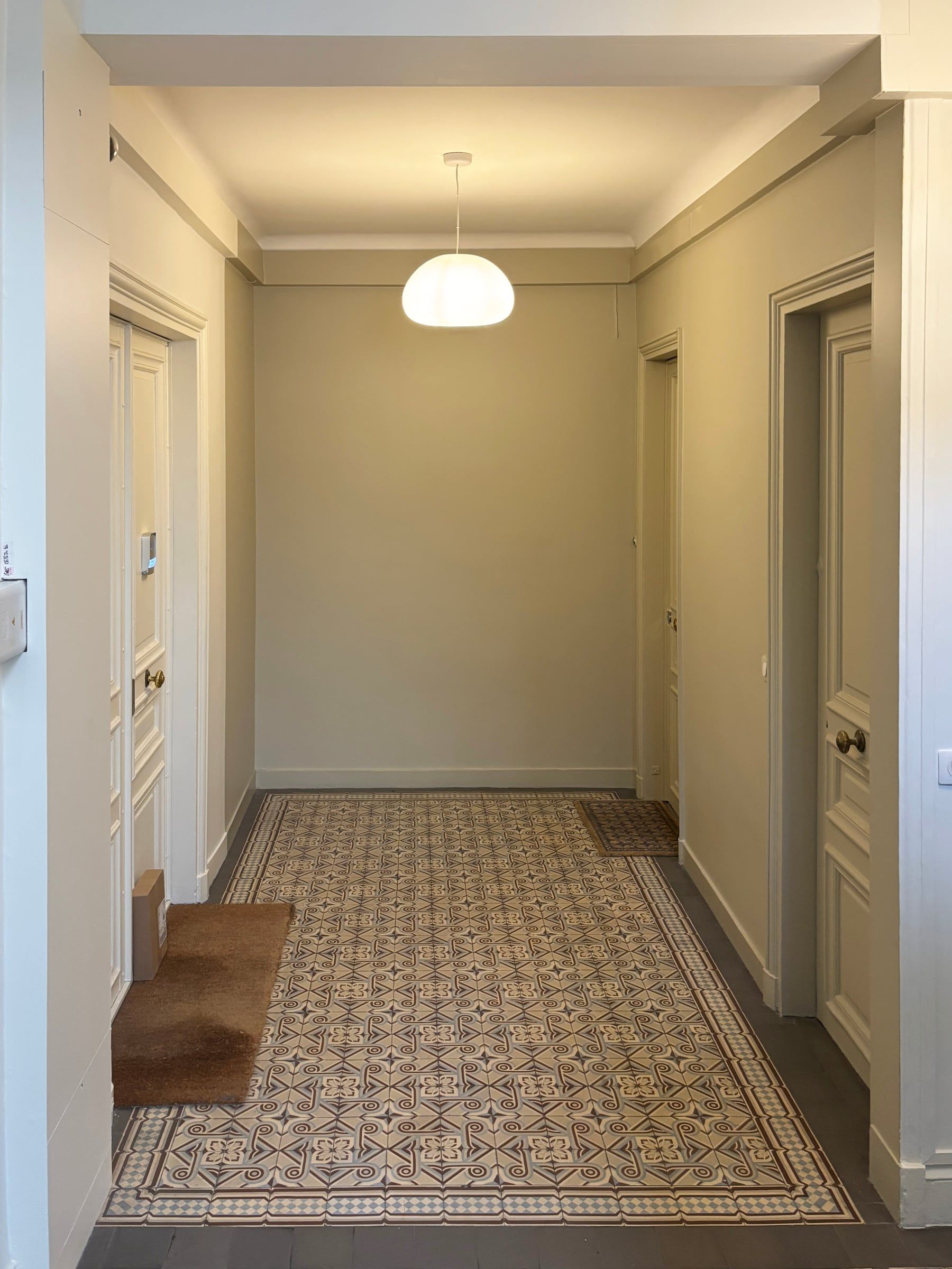 Circulation commune organisée autour d’un tapis de carreaux décorés, de portes anciennes peintes et d’un plafonnier globe.