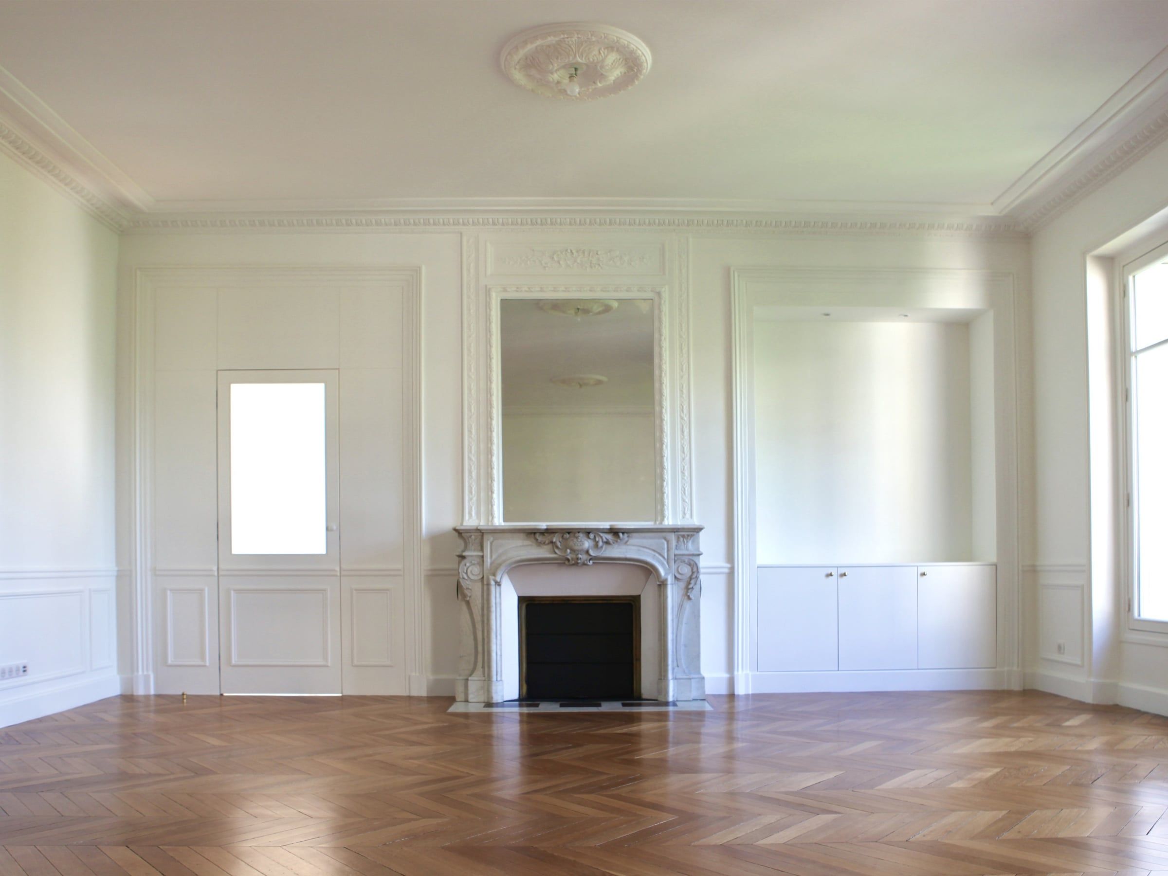 Séjour haussmannien aux boiseries blanches, cheminée en marbre à trumeau miroir et parquet en chevrons rénové par un architecte d'intérieur.
