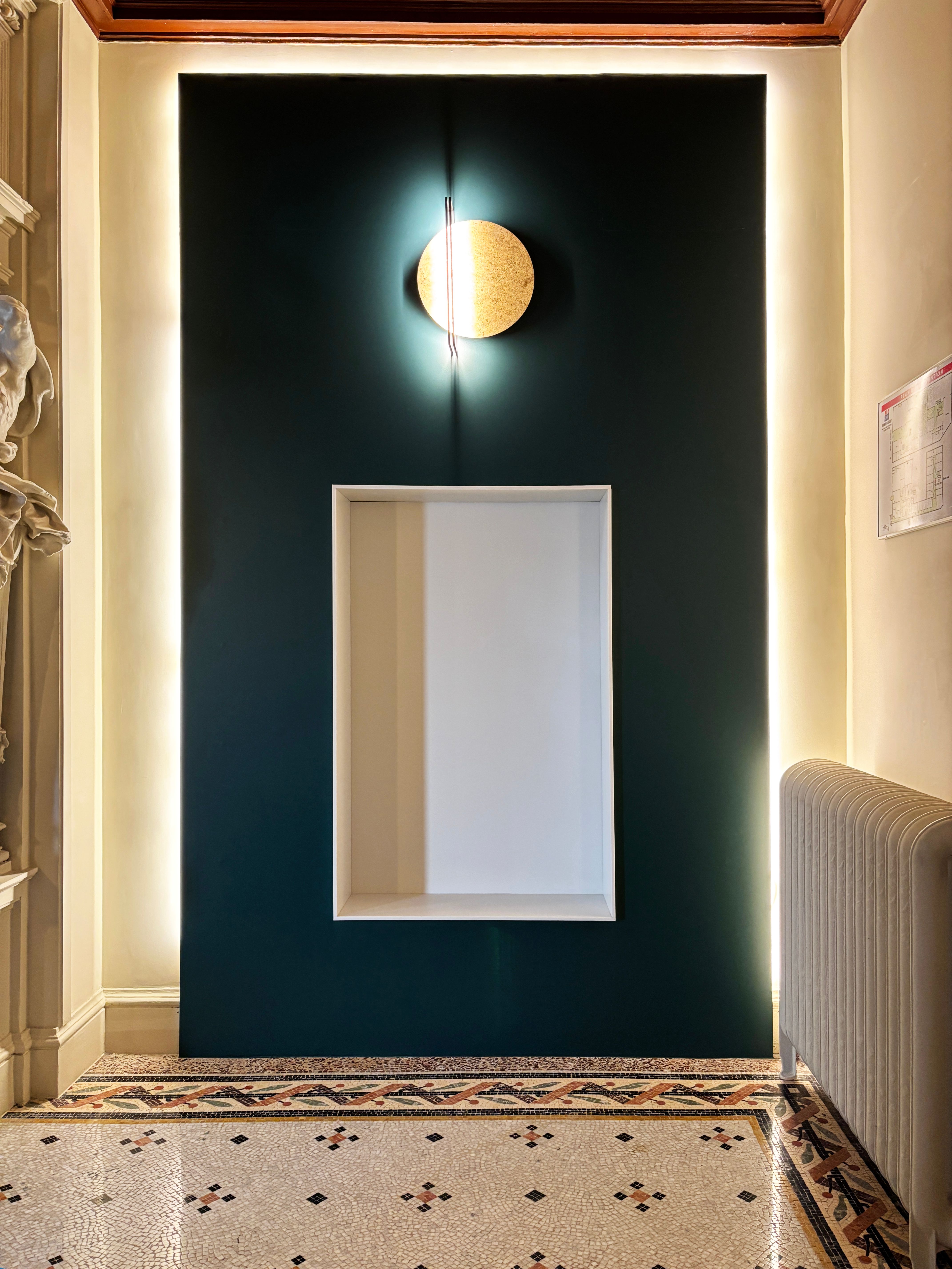 Panneau mural vert avec niche blanche et applique circulaire, éclairage périphérique pour la mise en lumière du hall commun.
