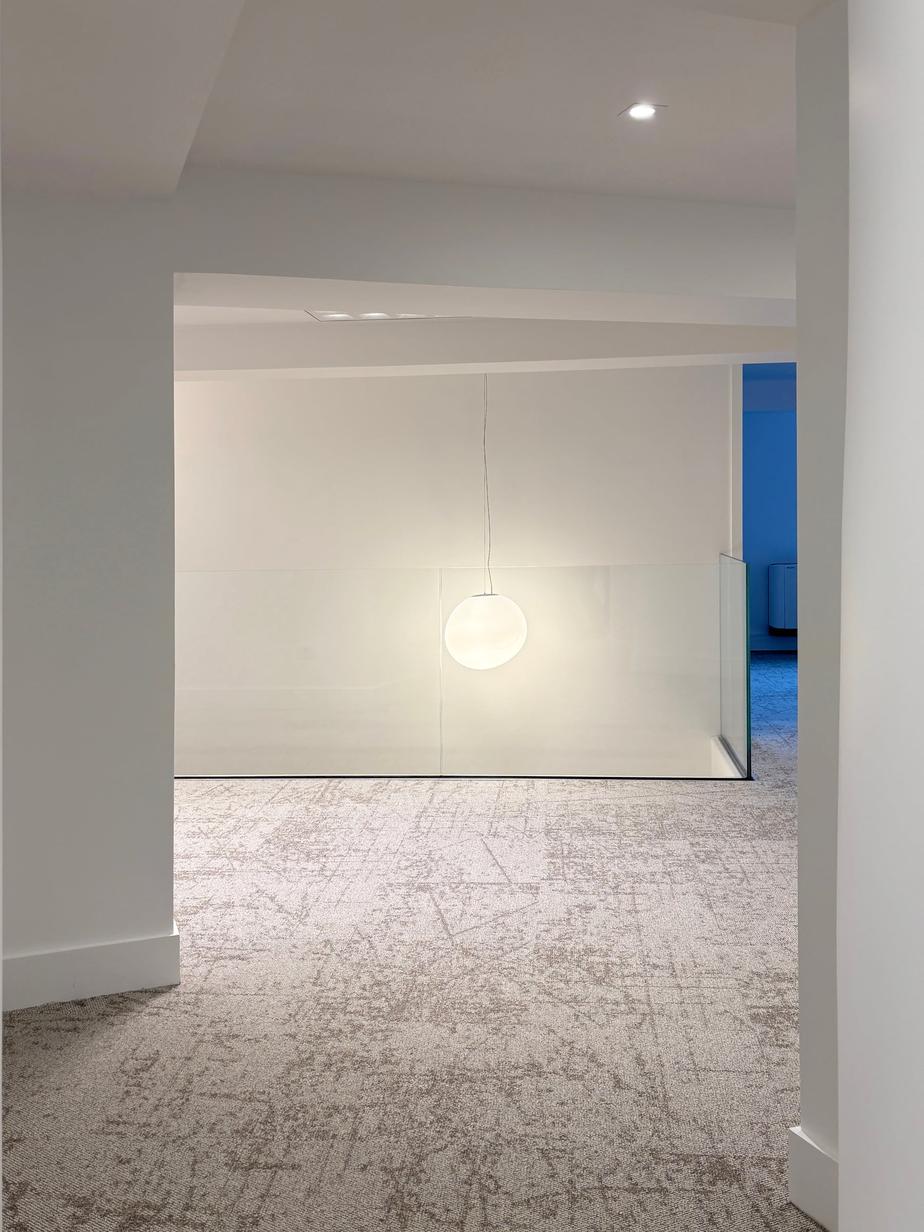 Circulation de bureaux en moquette claire avec suspension globe en verre opalin et trémie bordée d'un garde-corps en verre, espace de travail fluide
