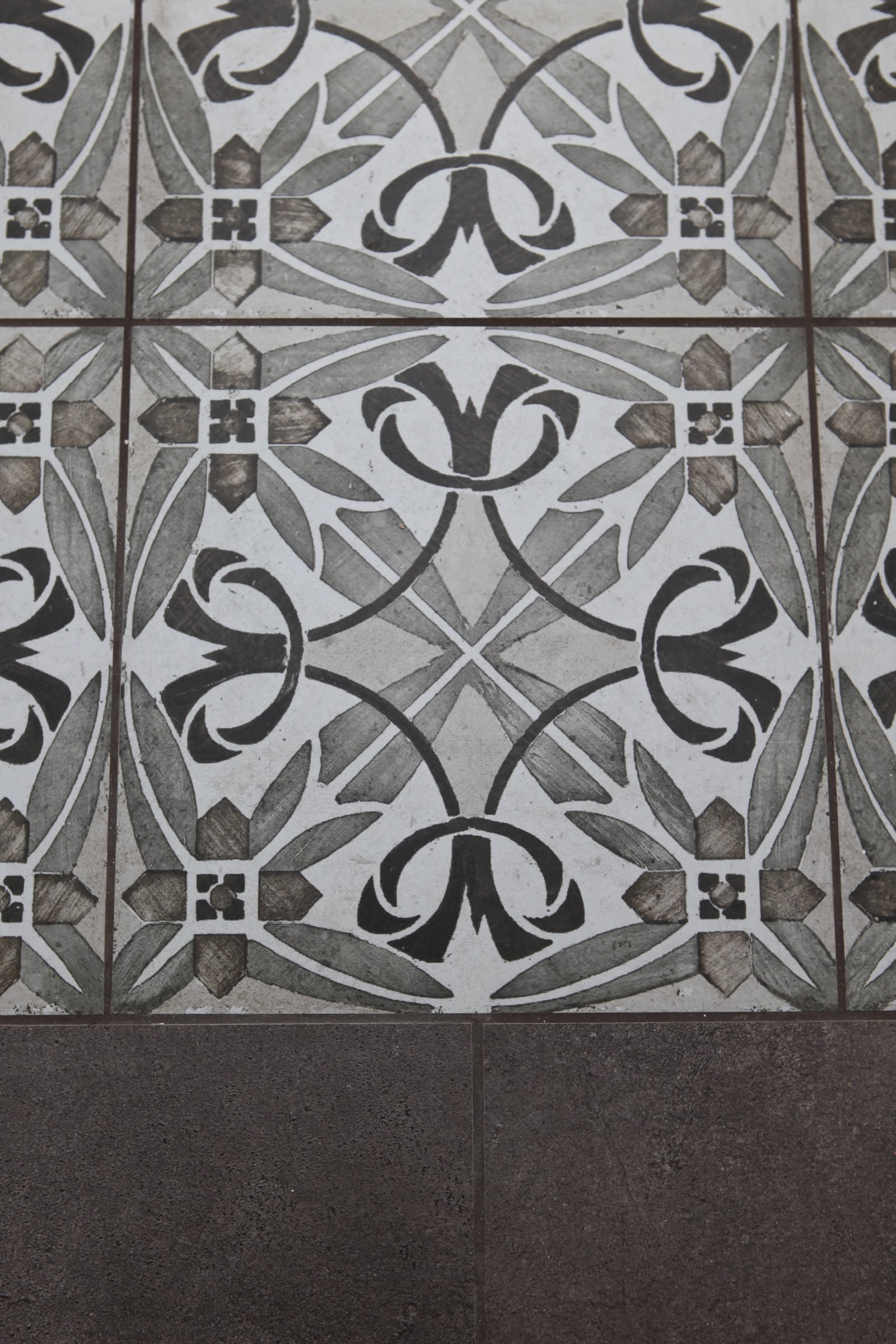 Détail d'un sol en carreaux de ciment à motif graphique noir et blanc en transition avec un dallage de pierre grise, agencement sur mesure.