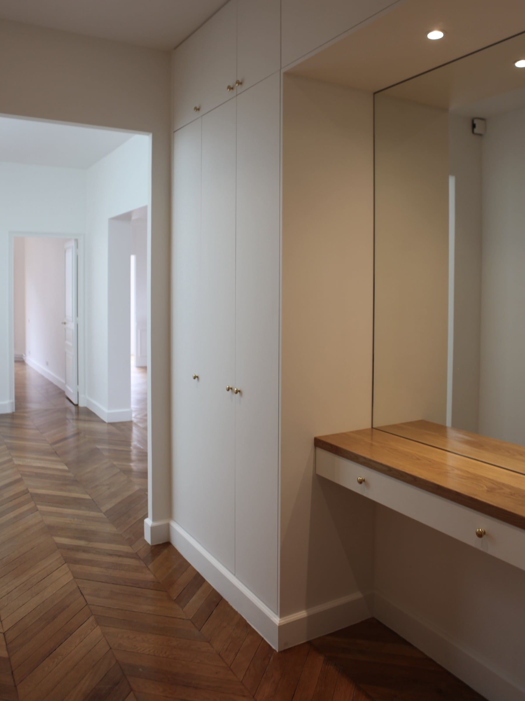 Entrée aux rangements toute hauteur sur mesure à poignées en laiton, console en chêne sous miroir et parquet en point de Hongrie, agencement sur mesure.