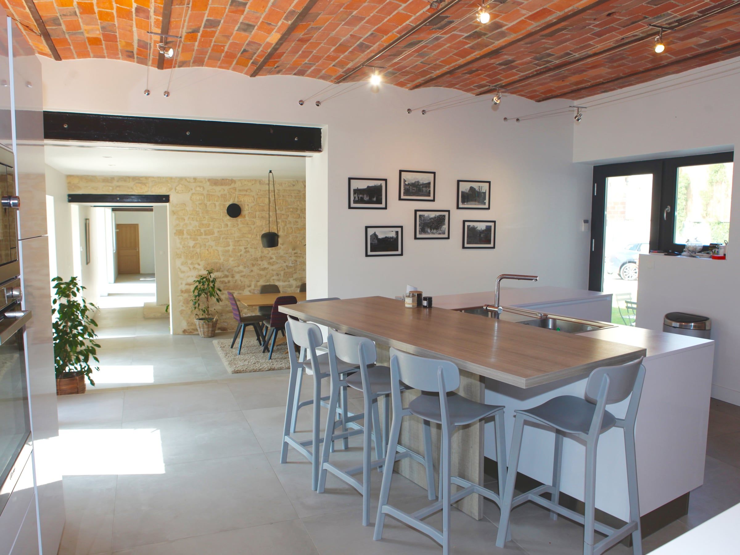 Rénovation de cuisine ouverte sous voûte en briques, avec grand îlot blanc à plan de travail en bois, évier intégré et tabourets hauts.