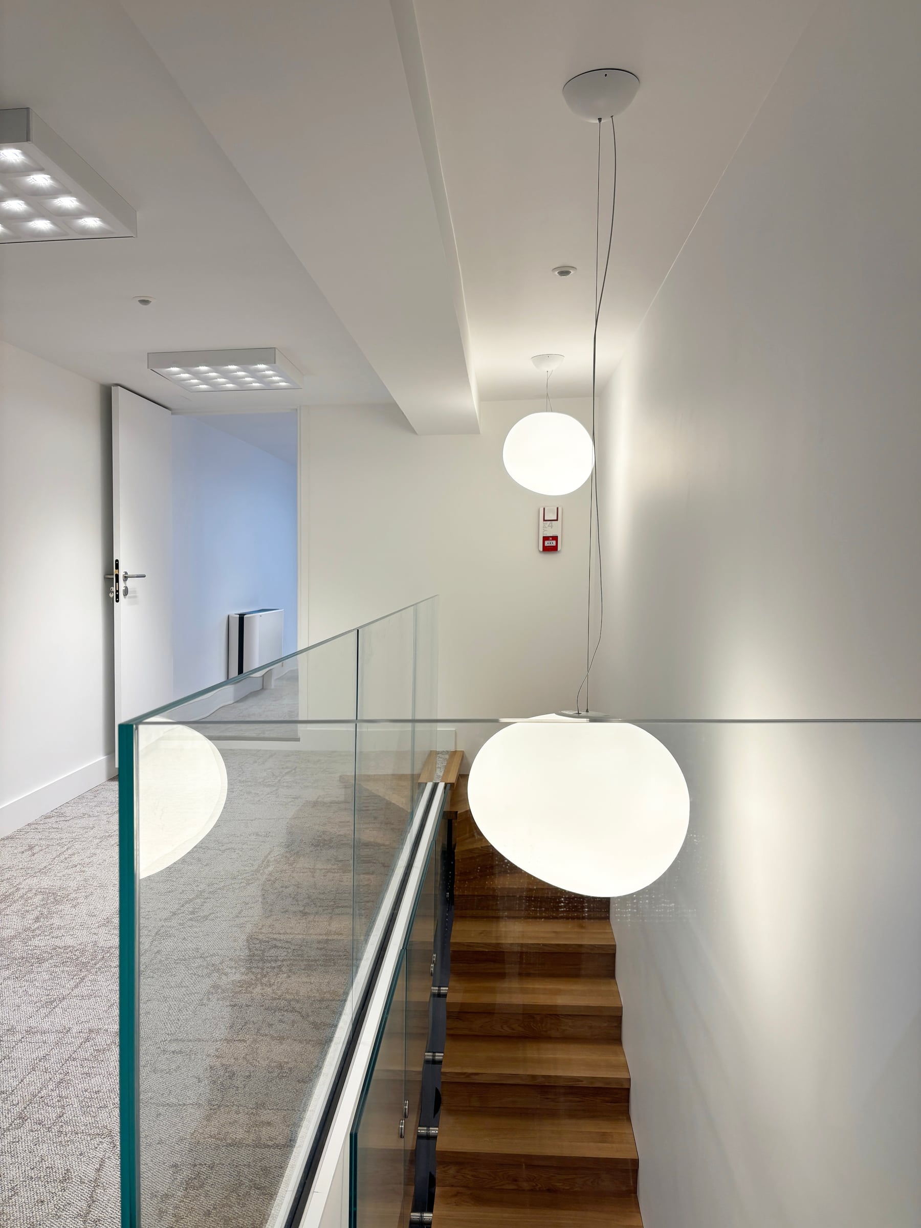 Cage d'escalier de bureaux avec marches en chêne, garde-corps en verre et suspensions globe en verre opalin, architecture intérieure tertiaire